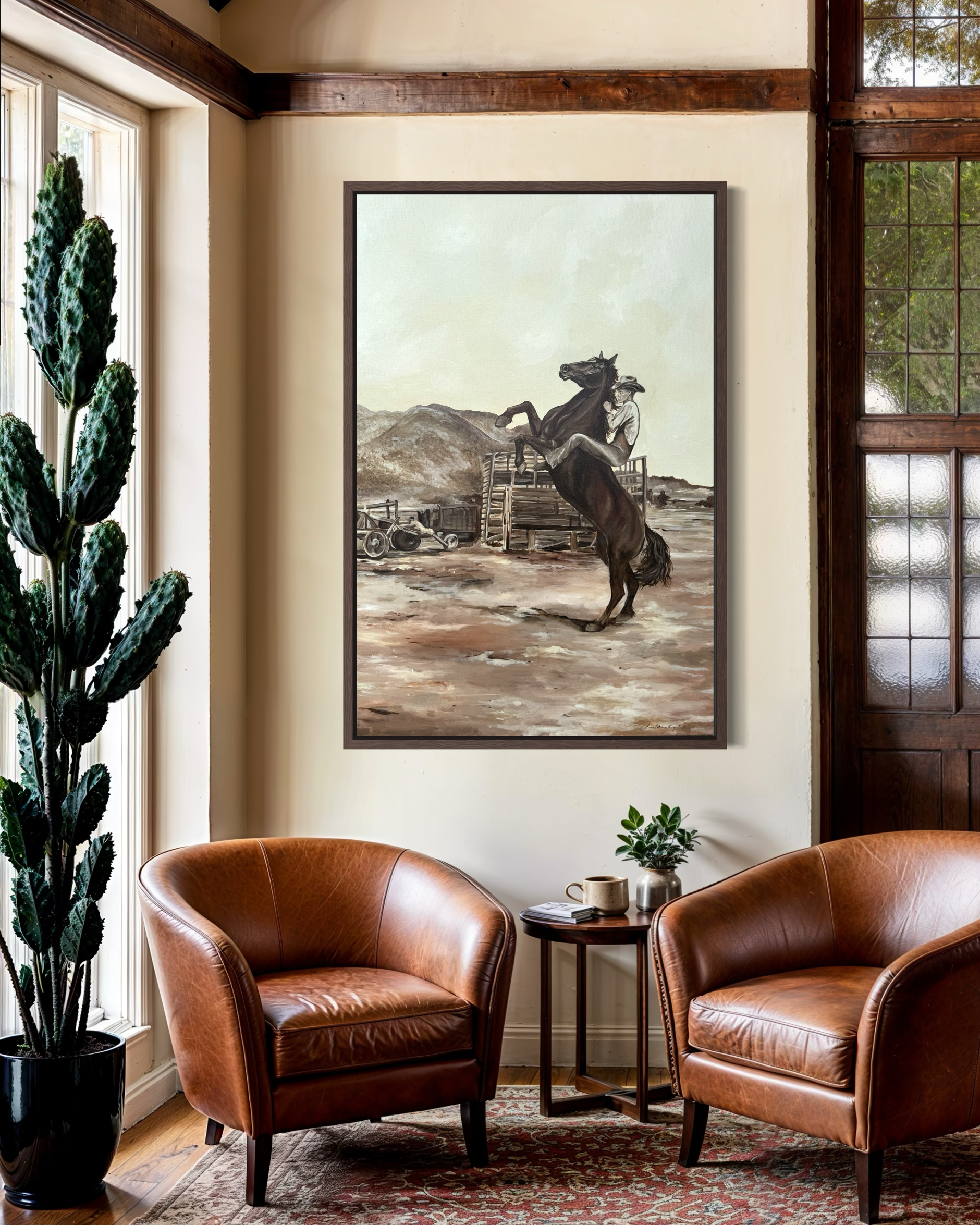 A cozy sitting area with three brown leather armchairs arranged around a small side table, a potted plant, and a large framed painting of a cowboy on a rearing horse in the background, with windows letting in natural light.