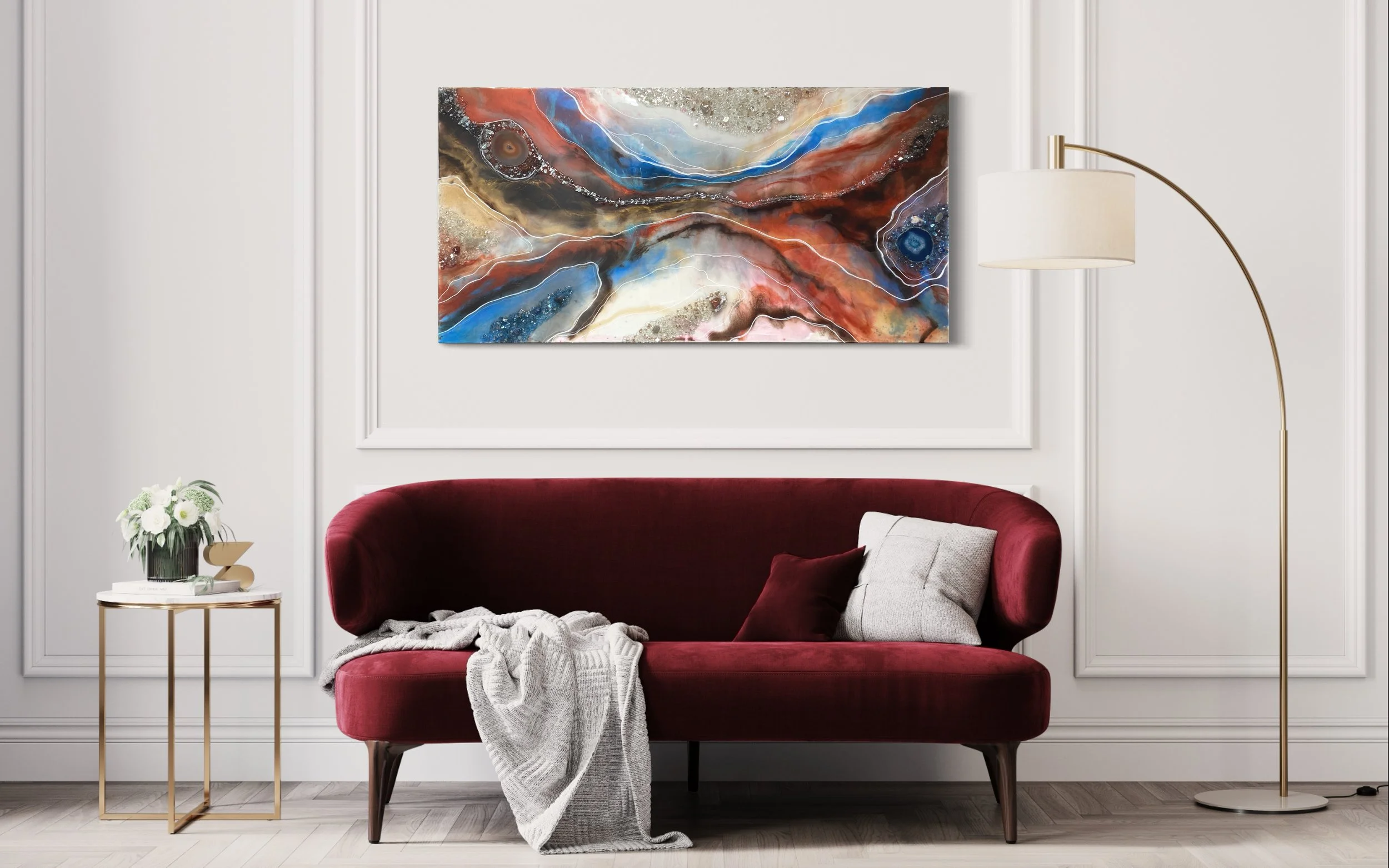 Abstract painting with swirling colors of red, blue, black, gold, and white hanging on a white wall in a modern living room.