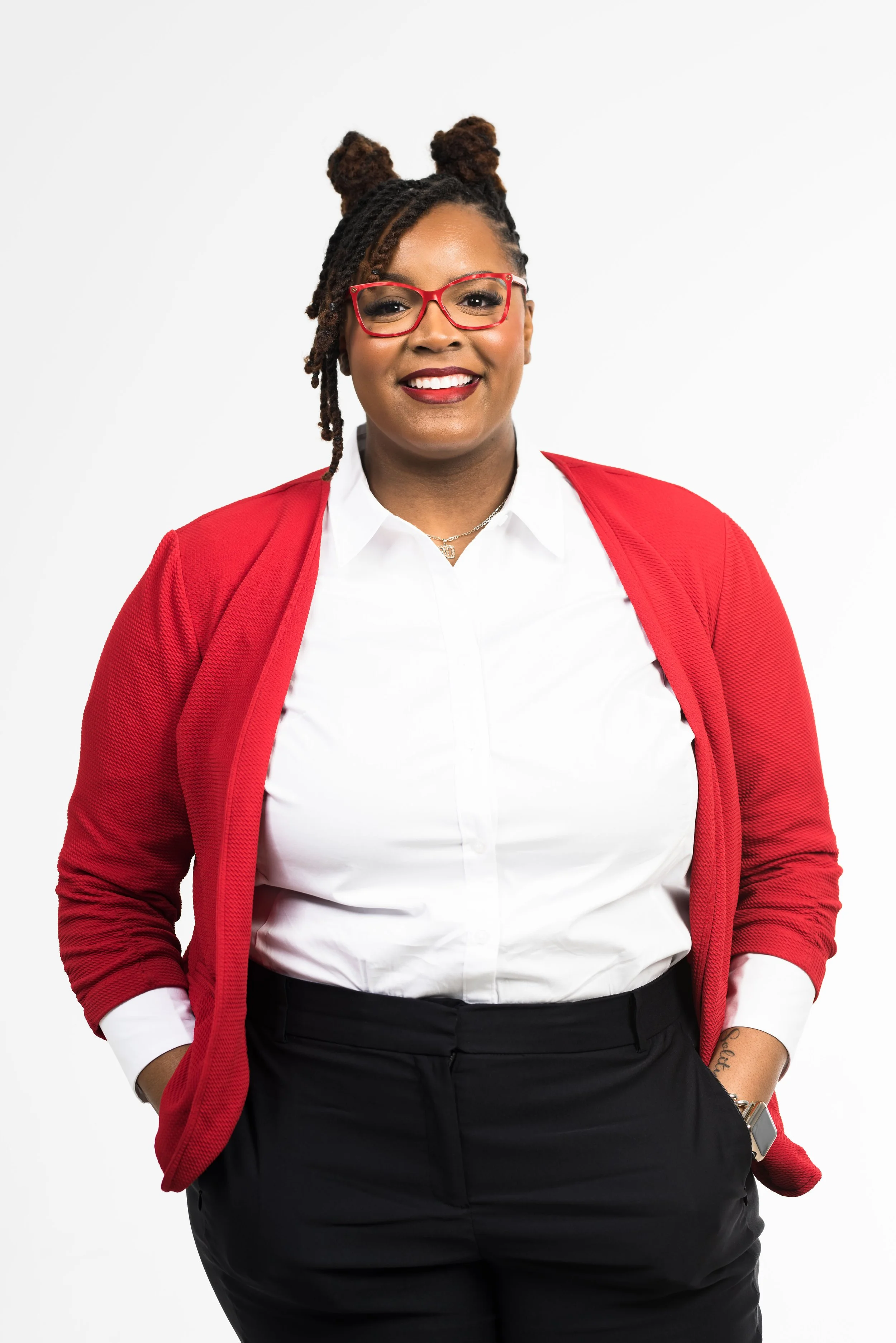 A smiling woman with glasses, wearing a red blazer over a white shirt and black pants, standing against a white background.