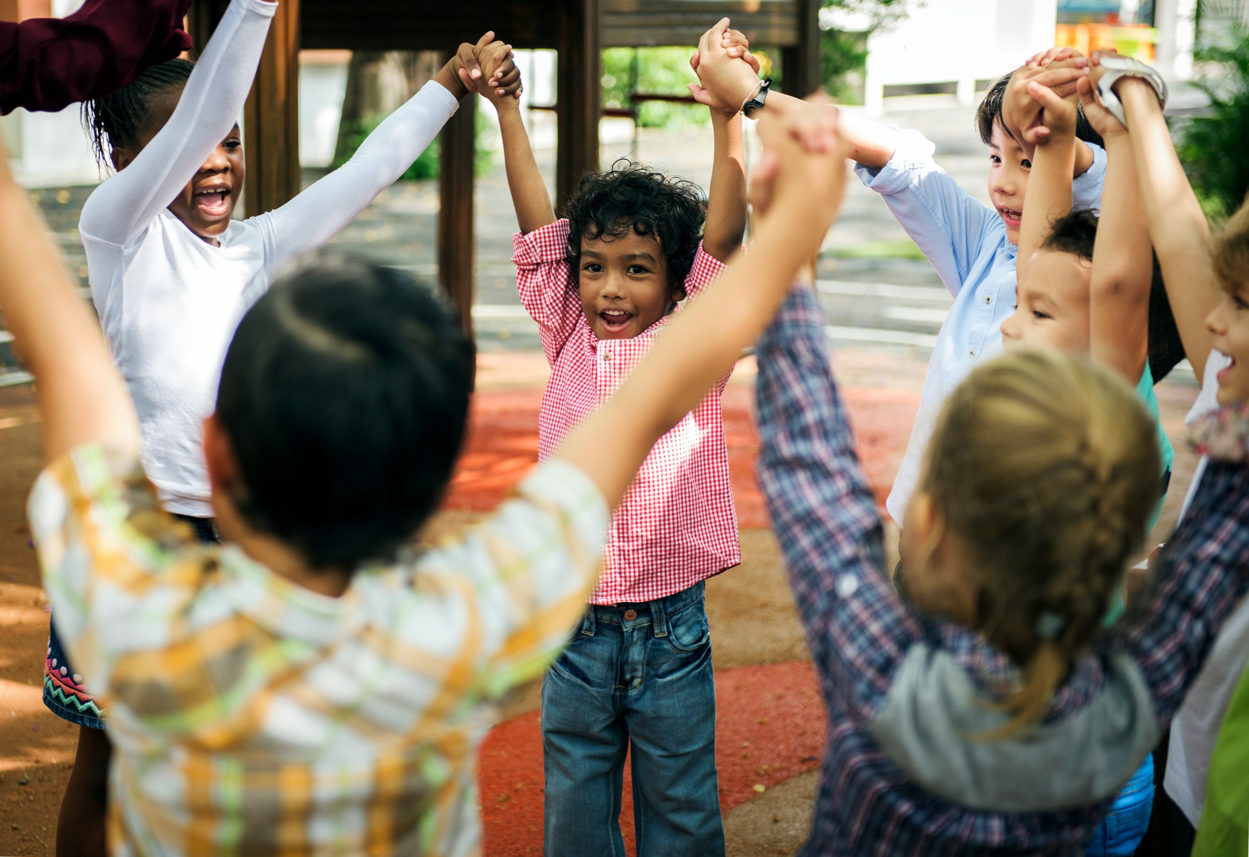 A diverse group of children holding hands and forming a circle, playing and smiling outdoors.