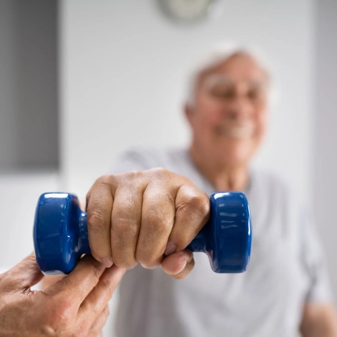 Older man smiling as he takes a blue dumbbell from someone.