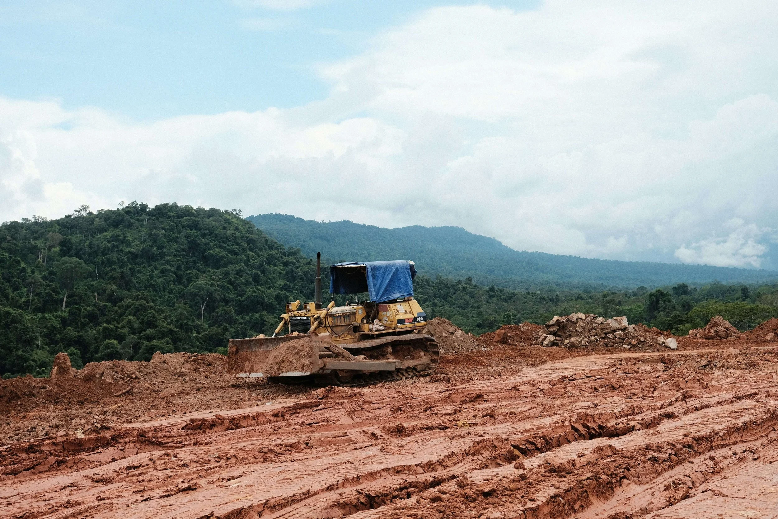 A bulldozer working on a large construction site for Alabama Landworks to develop land with dirt and rocks, surrounded by green hills and trees under a cloudy sky.