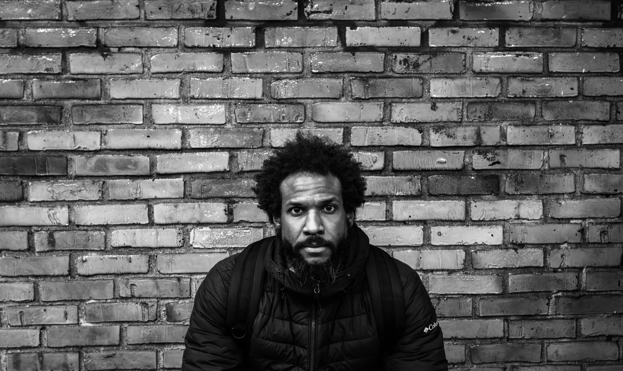 Author taru marcellus looks at camera with steady gaze while seated in front of a brick wall