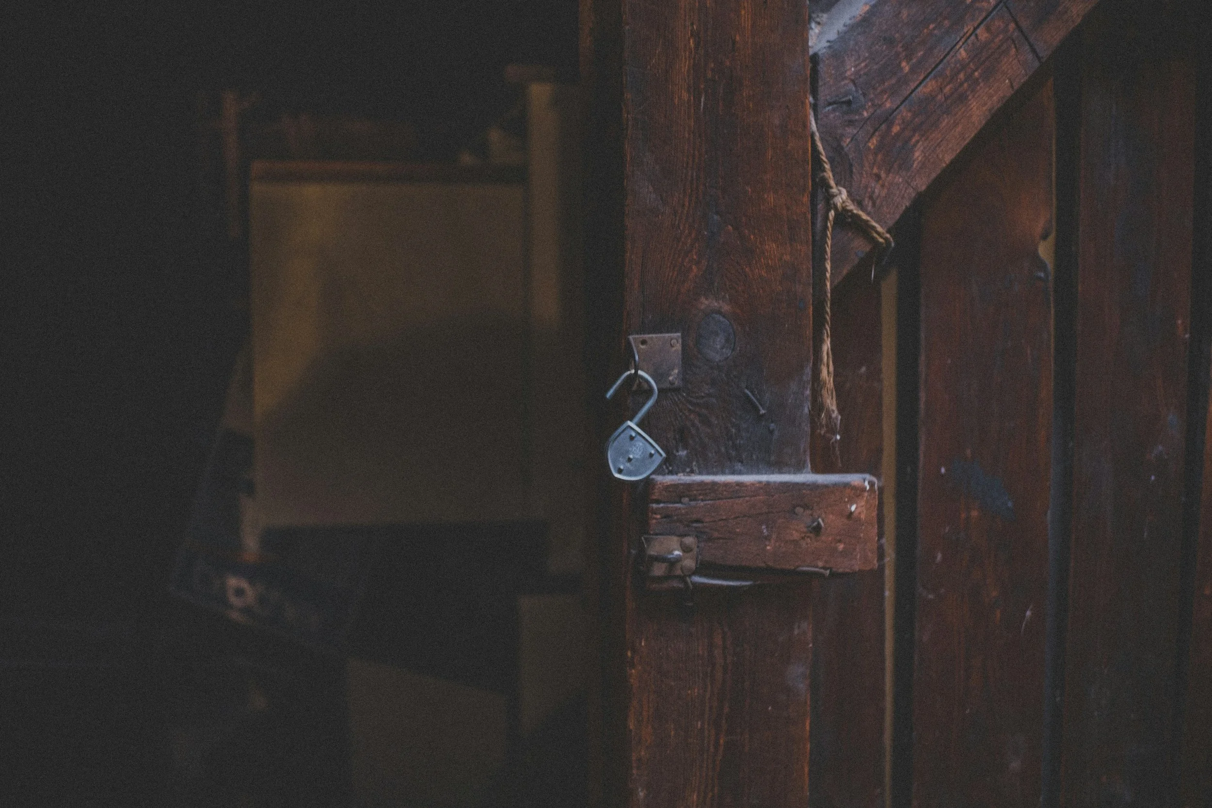 Close-up of a dark wooden door with a metal lock and a small, hollowed-out black padlock hanging from a metal hook.