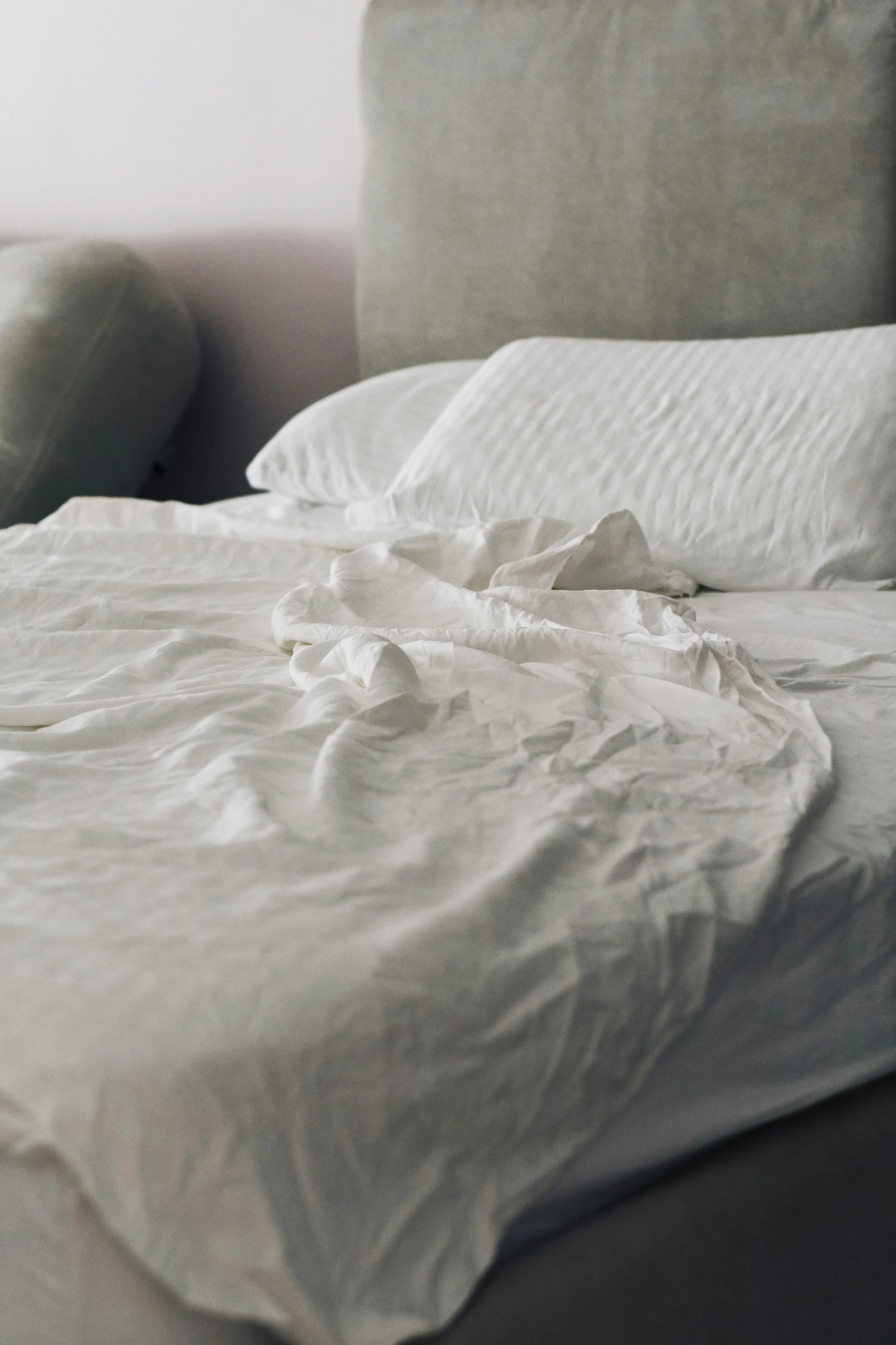 Unmade bed with white sheets, pillows, and crumpled bedding in a softly lit room.