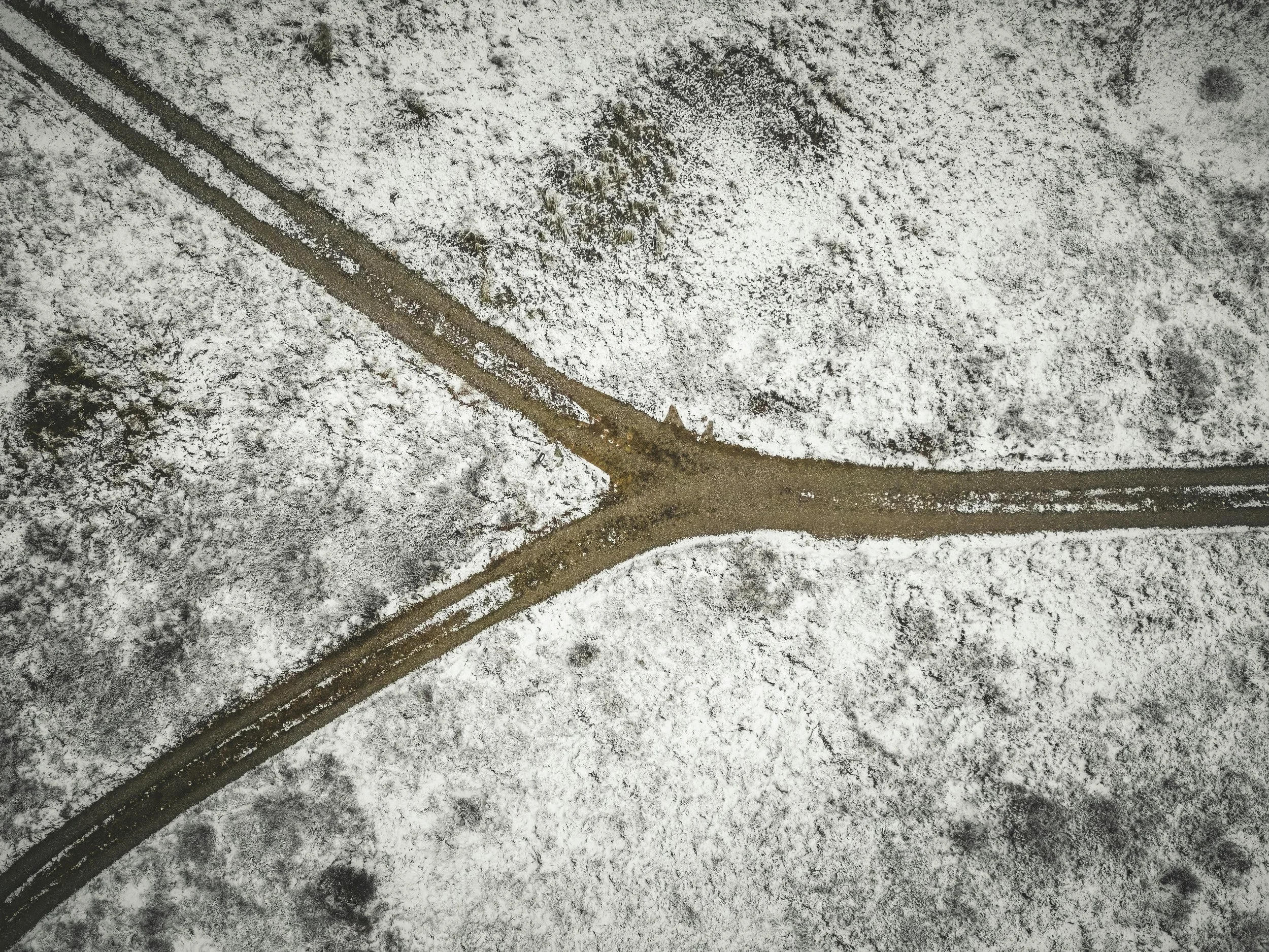 An aerial view of a snow-covered landscape with a Y-shaped dirt road splitting into two directions.