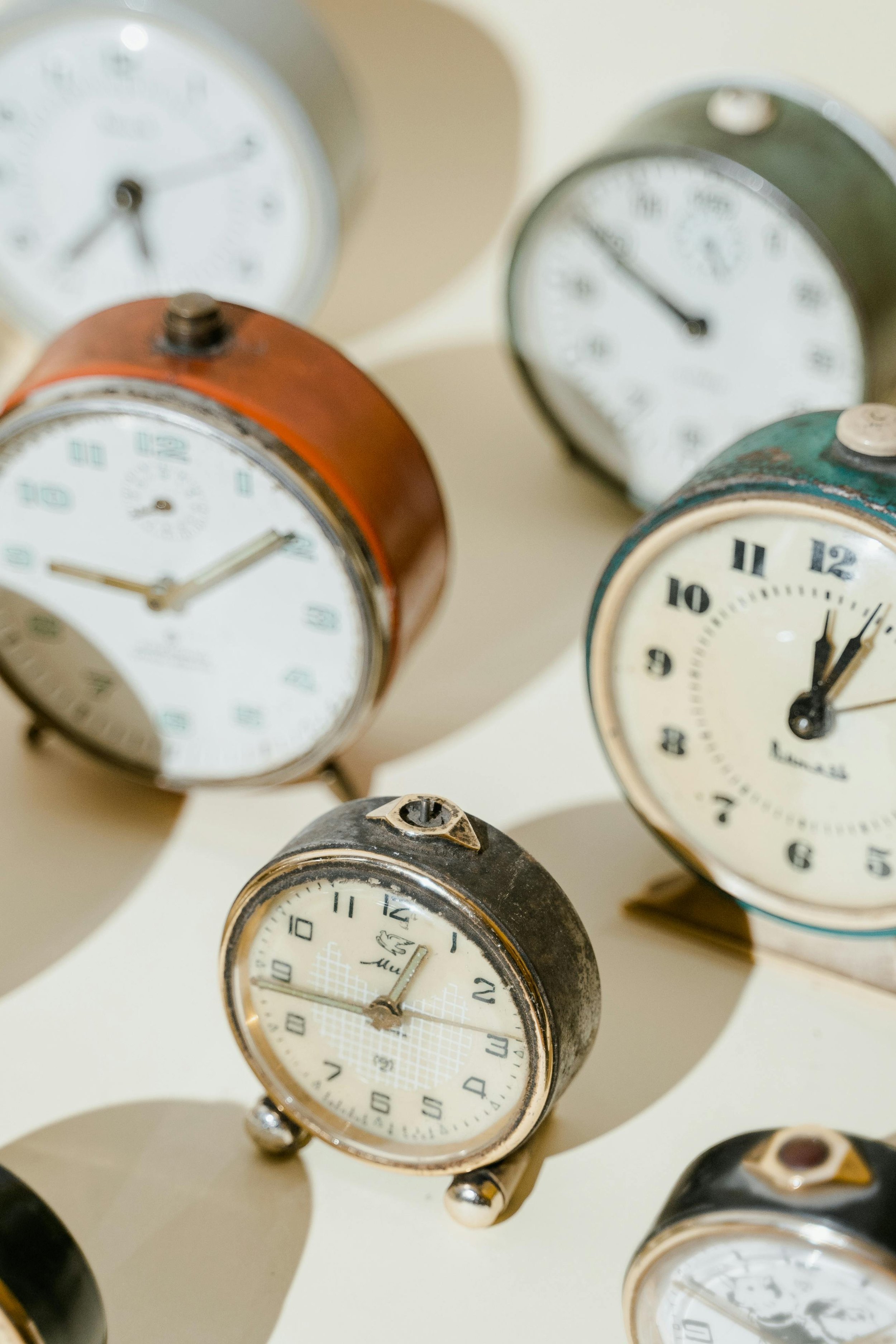 Multiple vintage alarm clocks in various colors and sizes, arranged on a white display surface.