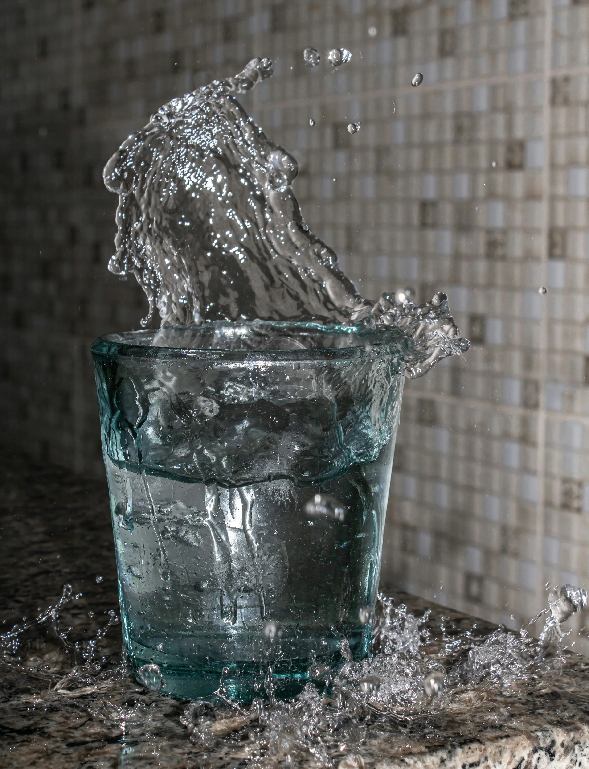 A glass of water with water splashing out as an ice cube is dropped in.