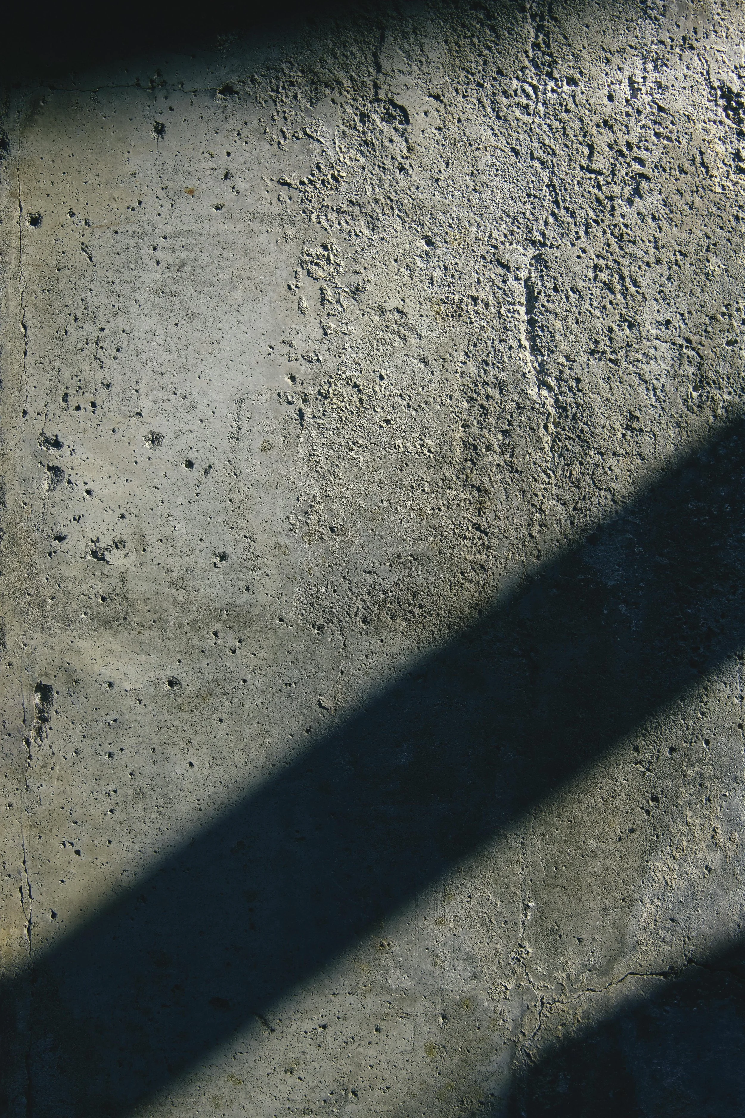 Close-up of a rough, textured concrete wall with shadows cast across it.