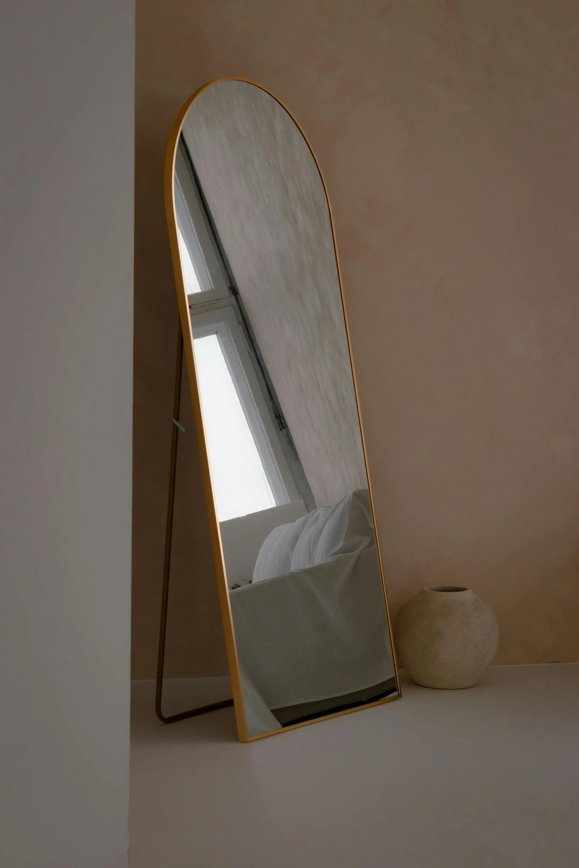 A tall, curved mirror with a yellow frame reflecting a bed and a window.