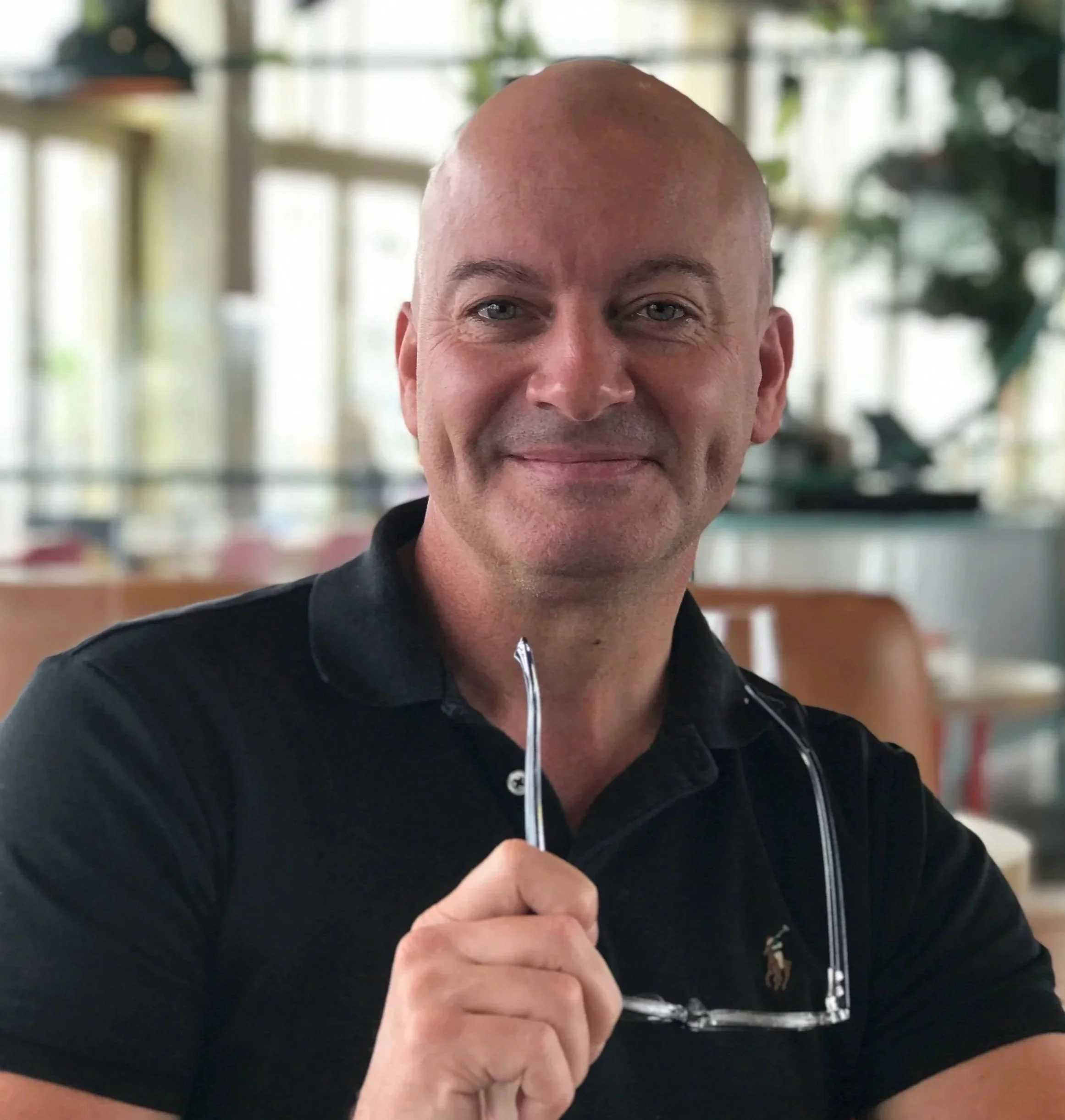 A man with a shaved head and blue eyes is holding a small needle and syringe, preparing to inject himself.