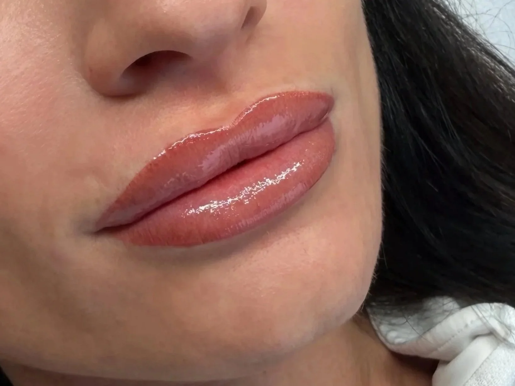 Close-up of a woman's lips with glossy, nude-colored lipstick.