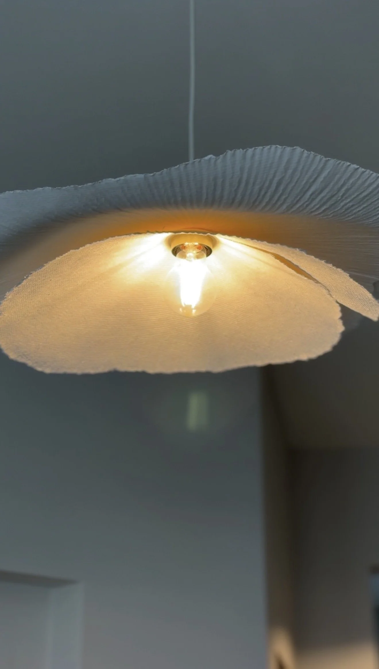 Close-up of a ceiling light fixture with an exposed bulb illuminated, partially covered by a torn piece of paper or fabric.