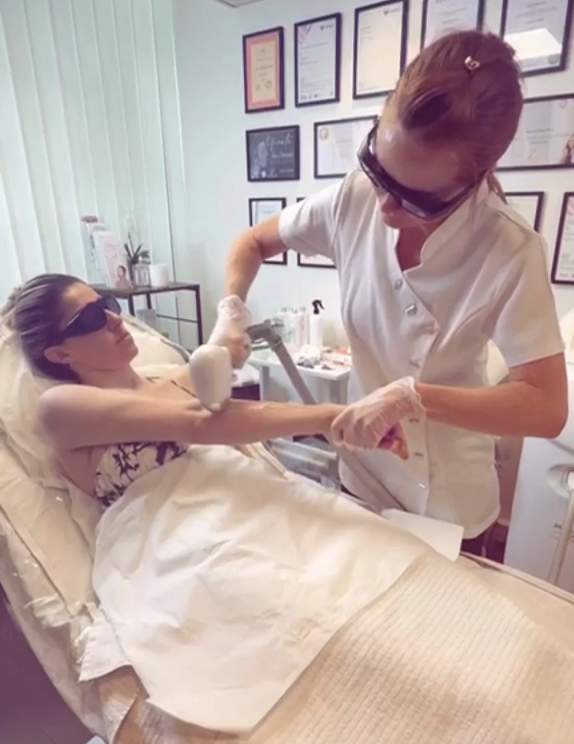 A woman lying on a medical bed, receiving laser hair removal treatment from a professional in a clinical setting.