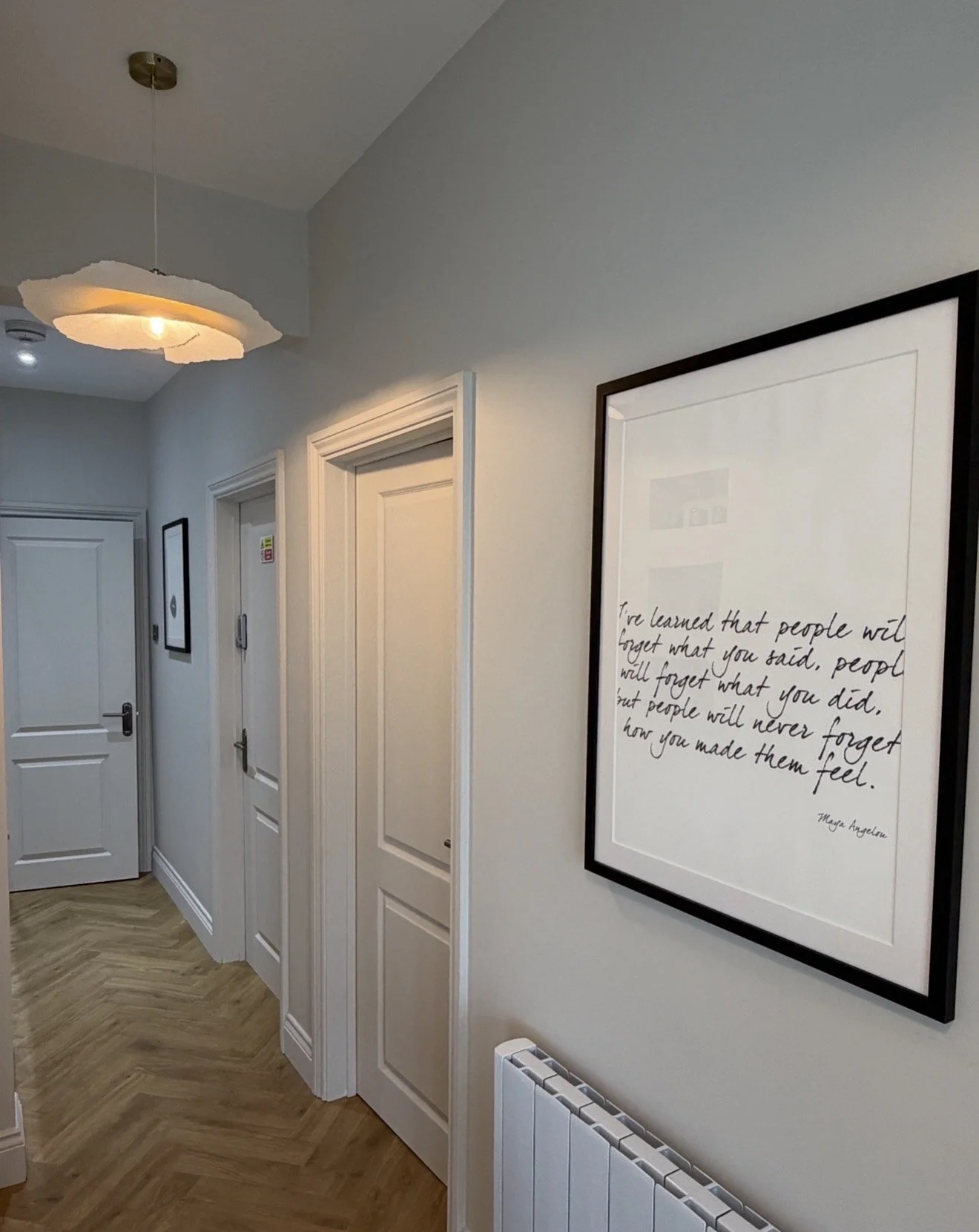 Hallway with white doors, a framed quote on the wall, and a ceiling light fixture.
