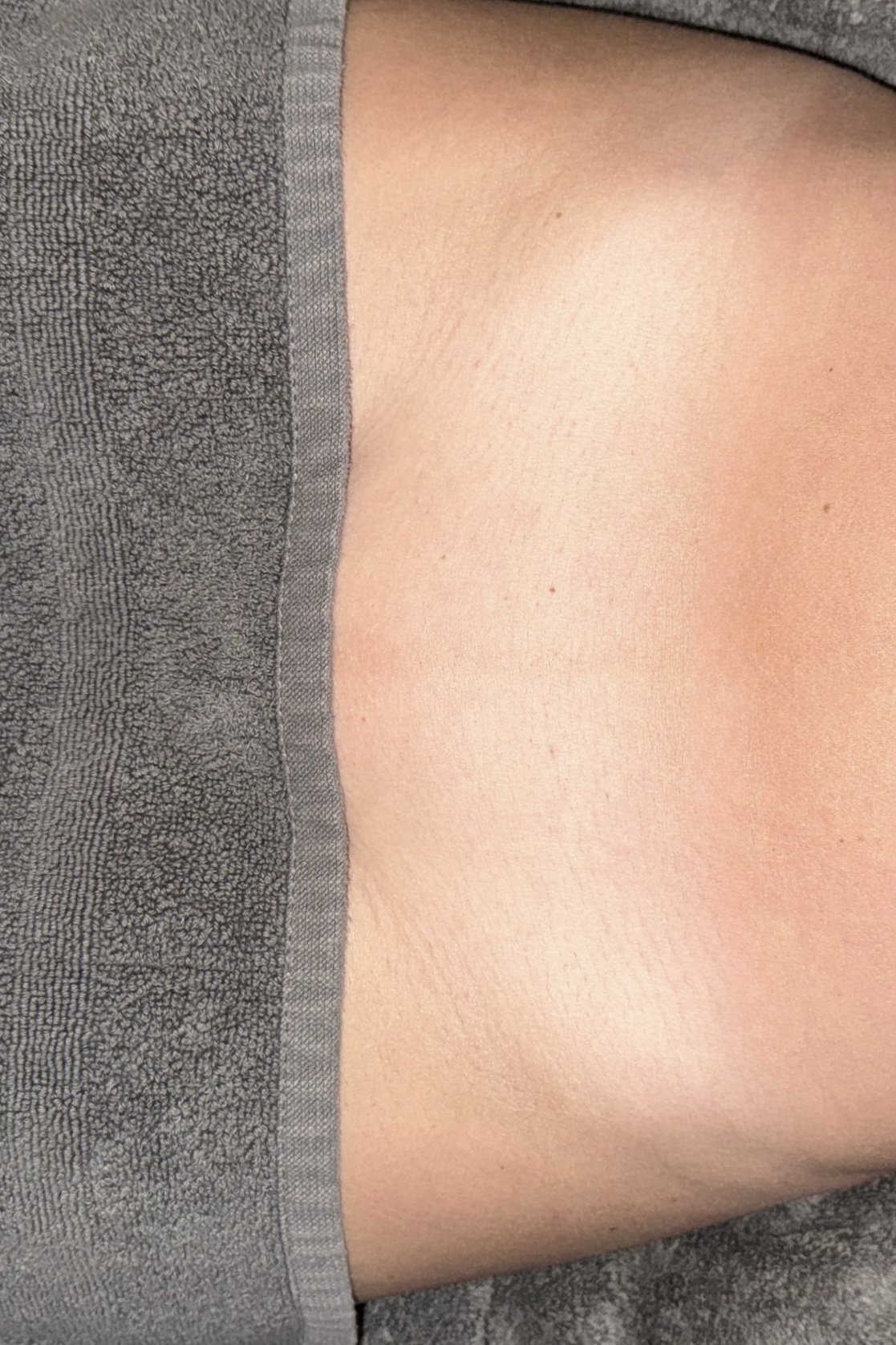 Close-up of a person's lower back in gray underwear, lying down on a gray towel.