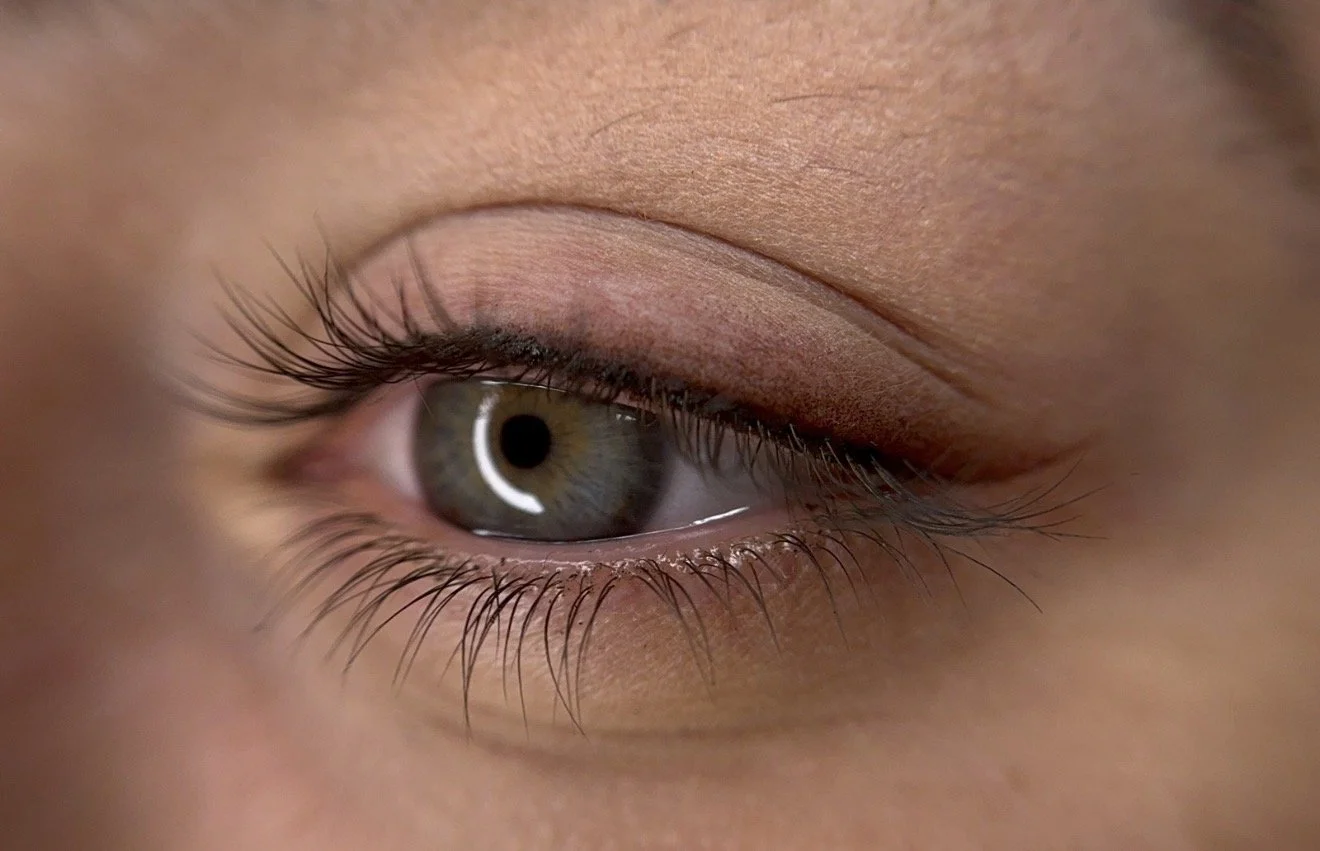 Close-up of a green eye with orange and brown accents, showing the eyelash detail and reflection of light.