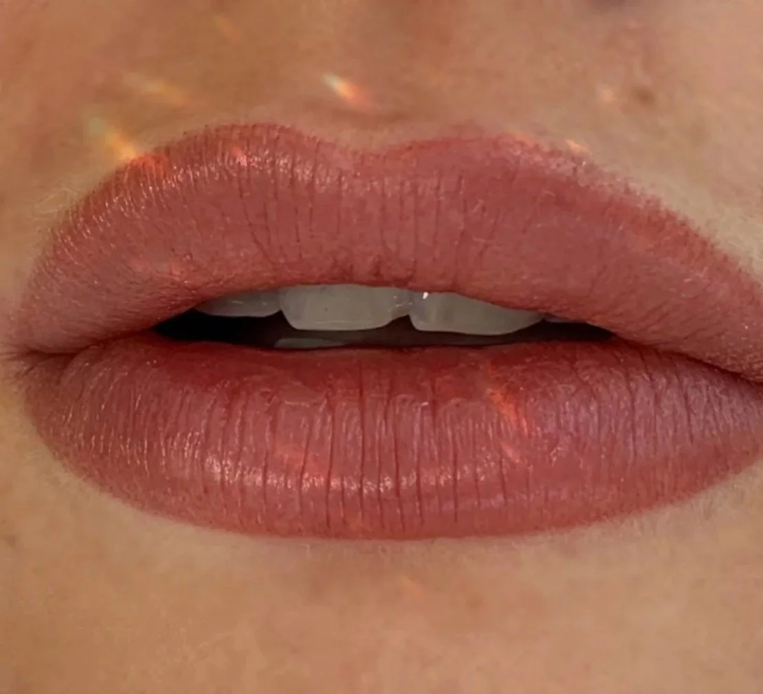 Close-up of lips with nude lipstick and visible teeth, slightly parted.