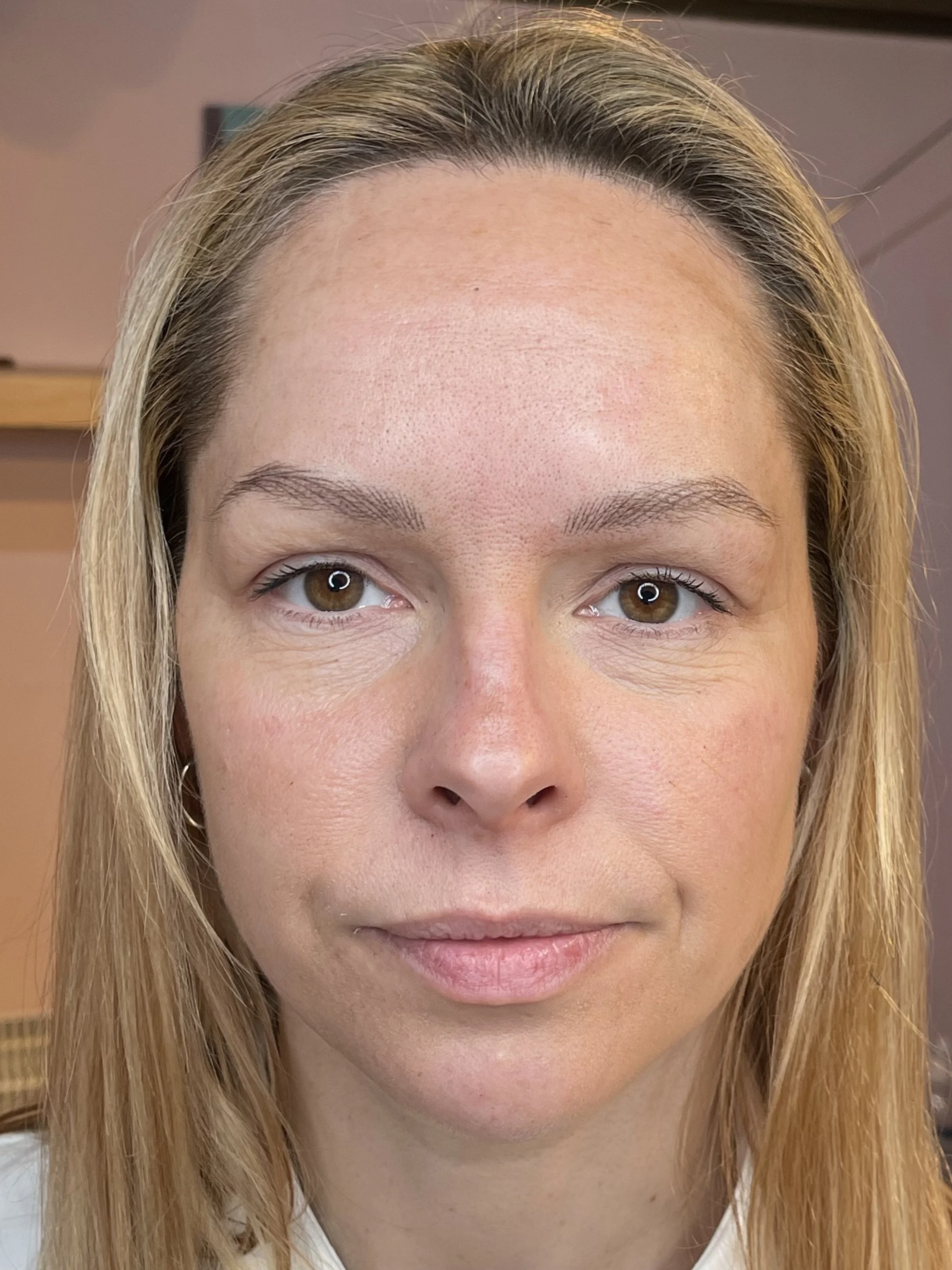 Close-up of a woman with light skin and long blonde hair, looking directly at the camera. Her face is centered in the image, with natural makeup and neutral expression.
