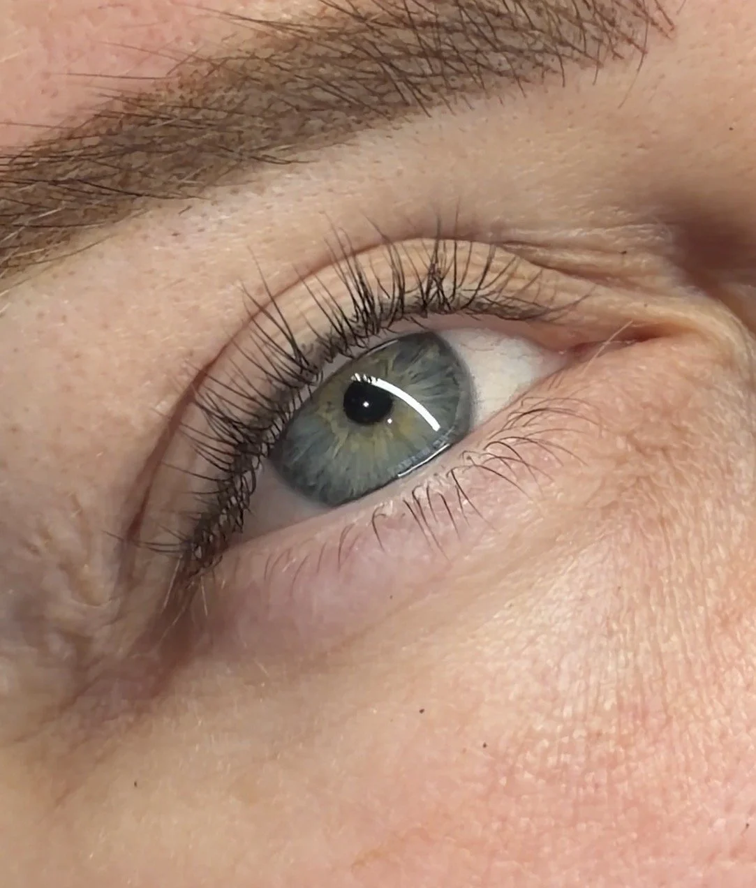 Close-up of a human eye with greenish-blue iris and long eyelashes.