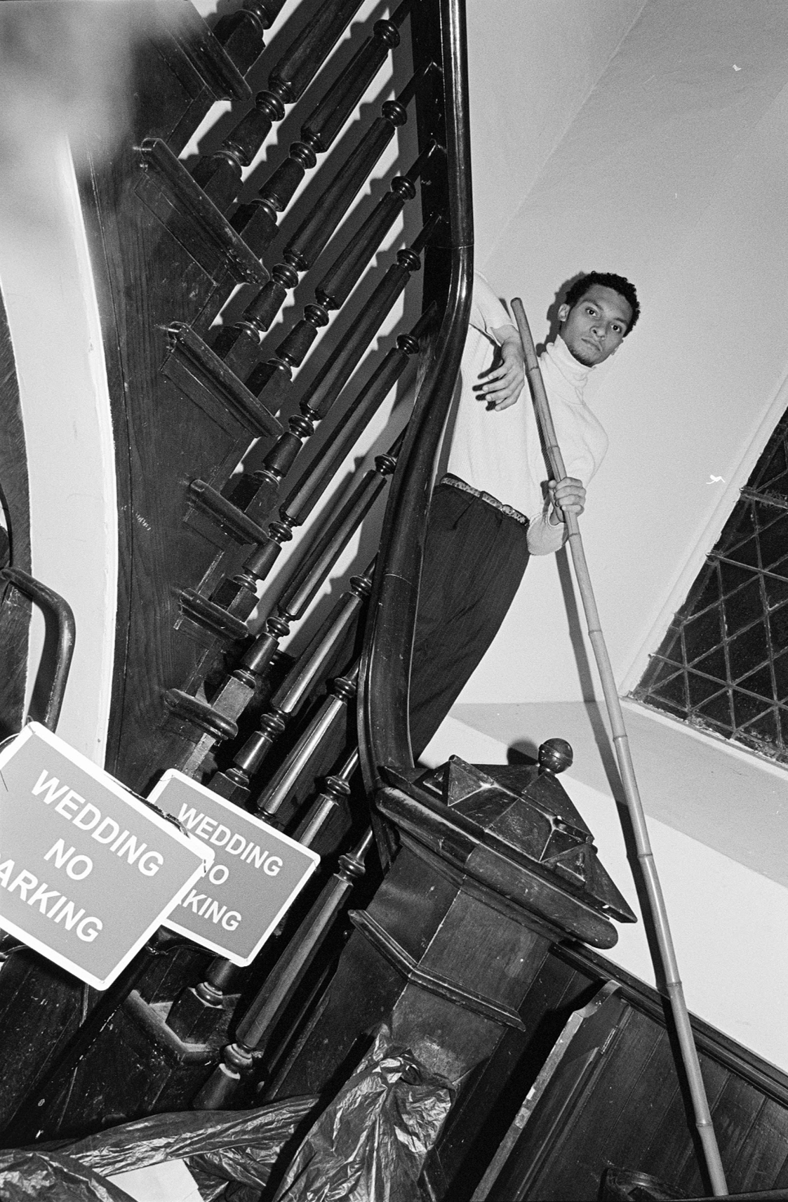 Man standing on staircase with a broom, looking at the camera, with wedding 'no parking' signs in the foreground.