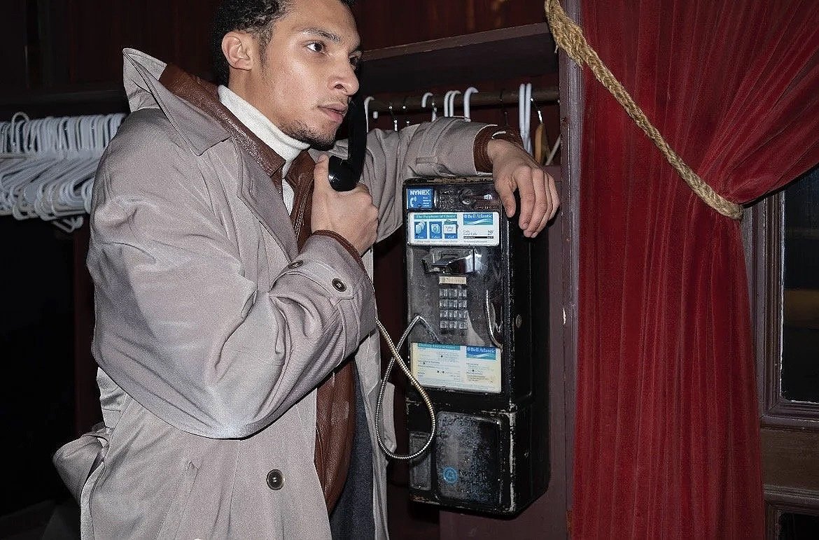 A man in a beige coat using a payphone.