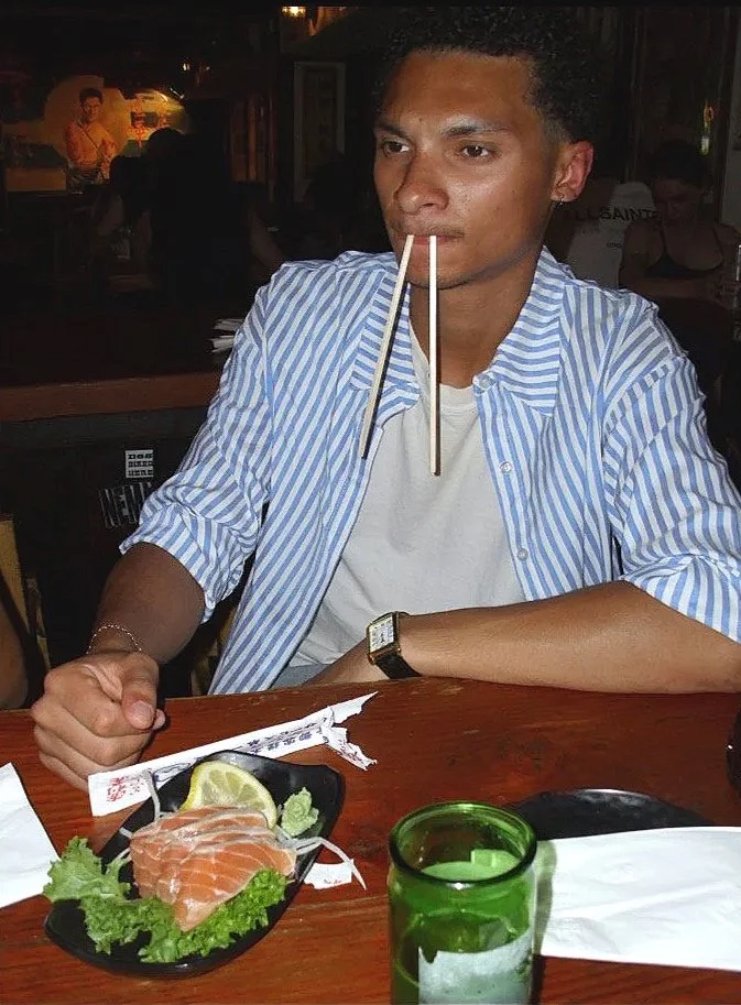 A man with chopsticks in his mouth sitting at a restaurant table.
