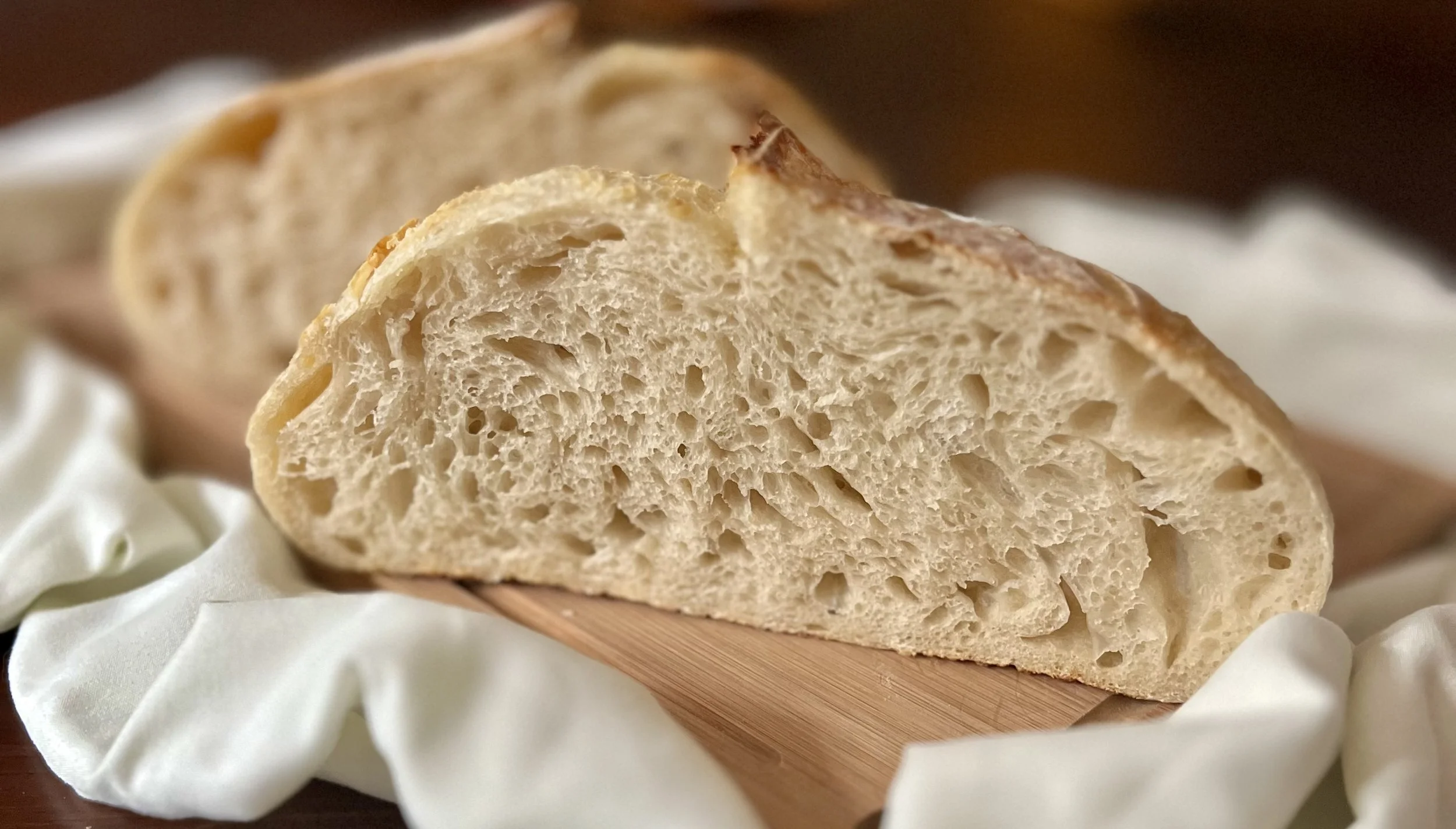 Close-up of a sliced loaf of bread on a wooden board, with a white cloth underside.
