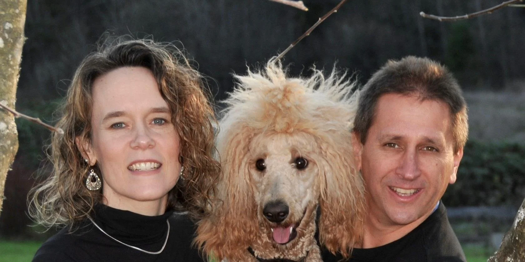 A woman, a man, and a poodle dog outdoors in a park or yard during daytime.