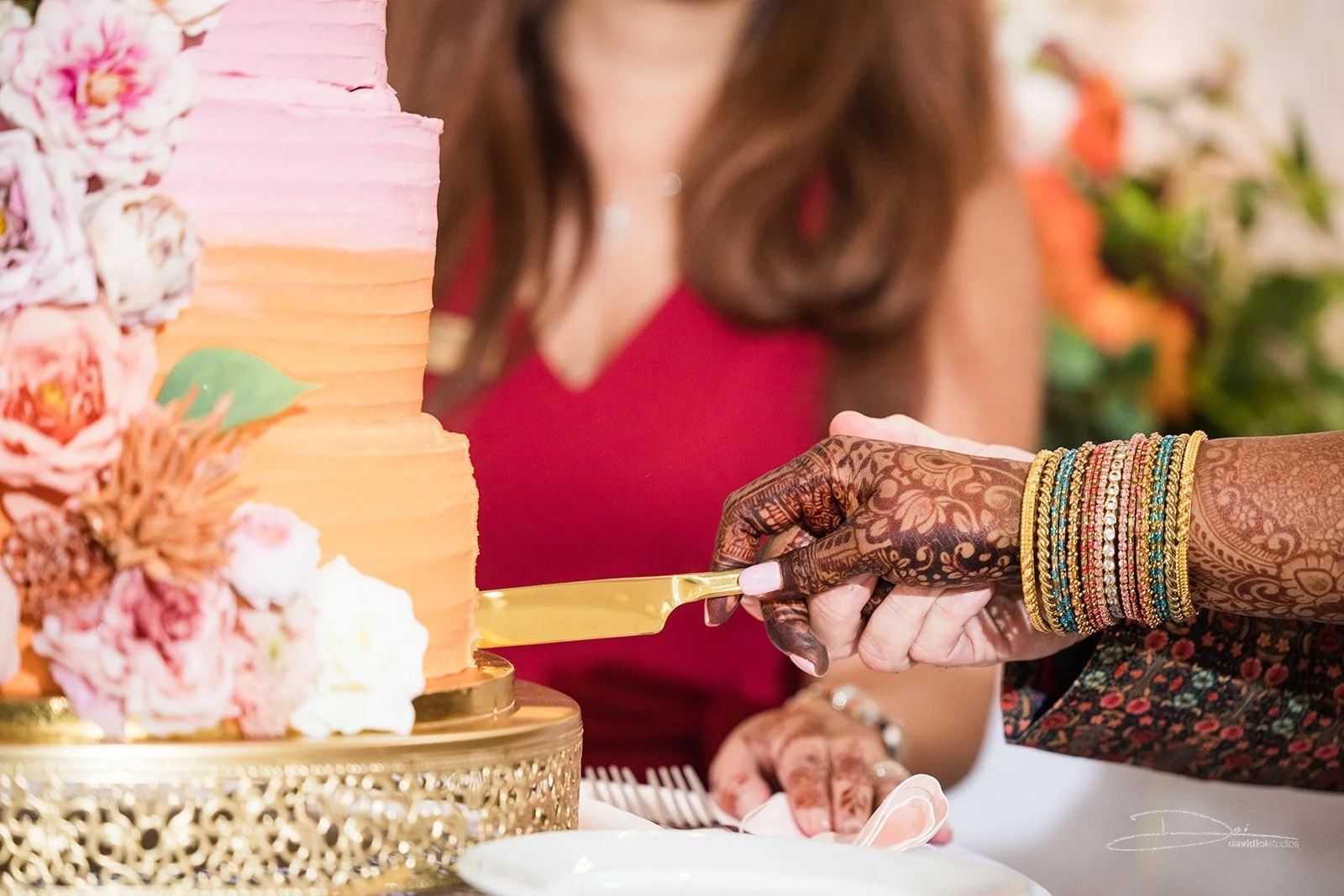 Close-up of a woman cutting a decorated rainbow-colored wedding cake with a gold knife during a celebration.