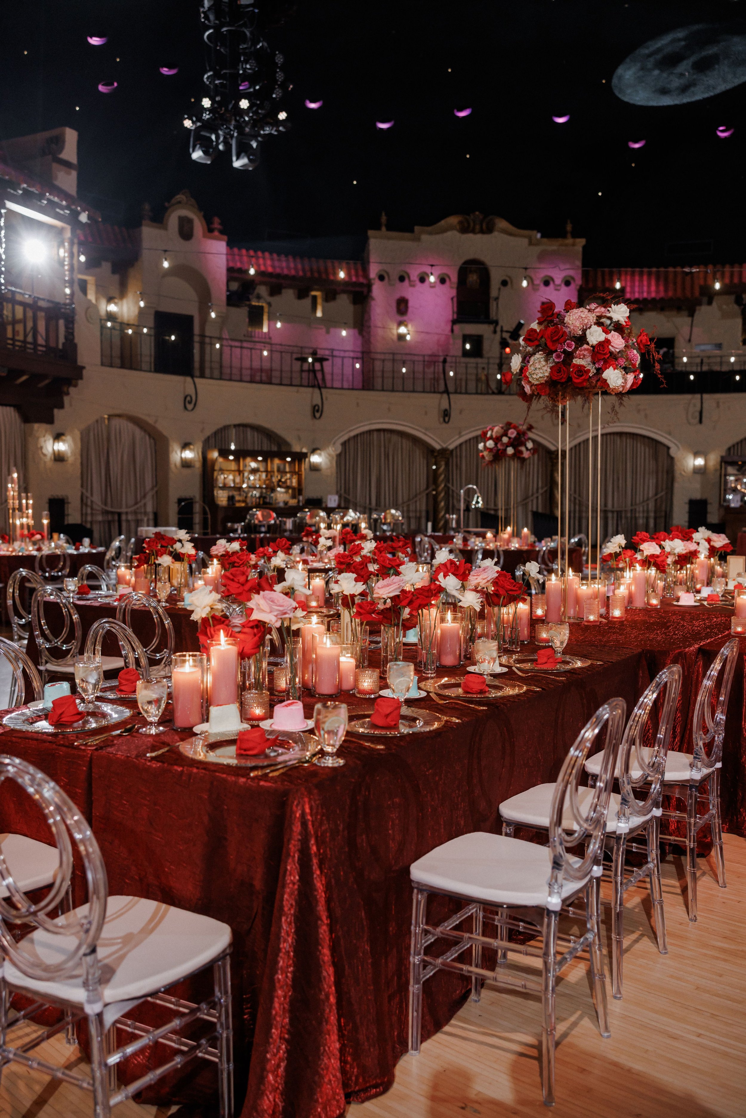 Elegant banquet hall decorated with red and pink flowers, candles, and luxurious table settings for a special event or wedding.