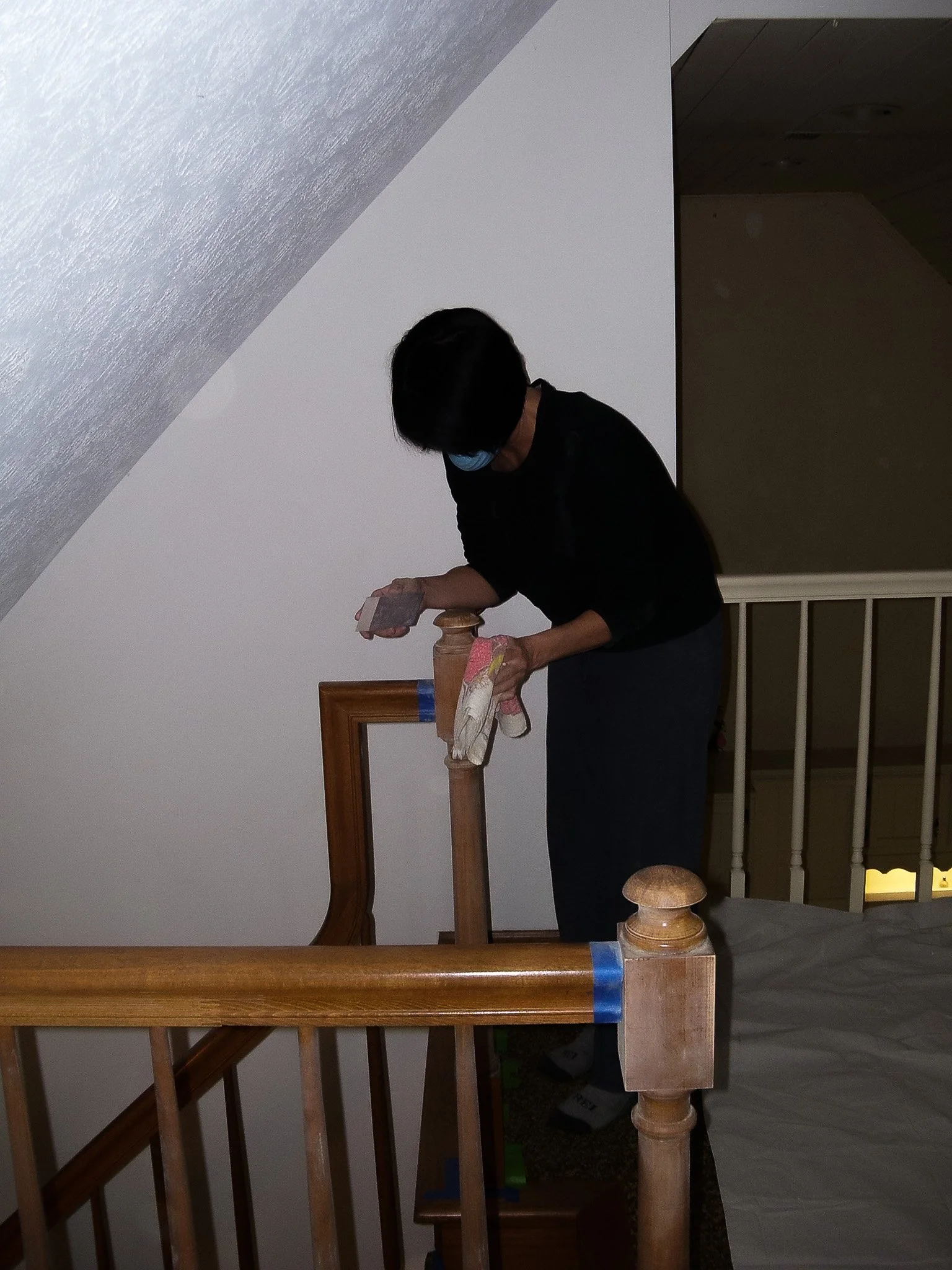 Person wearing a face mask working on a wooden staircase possibly sanding or painting it.