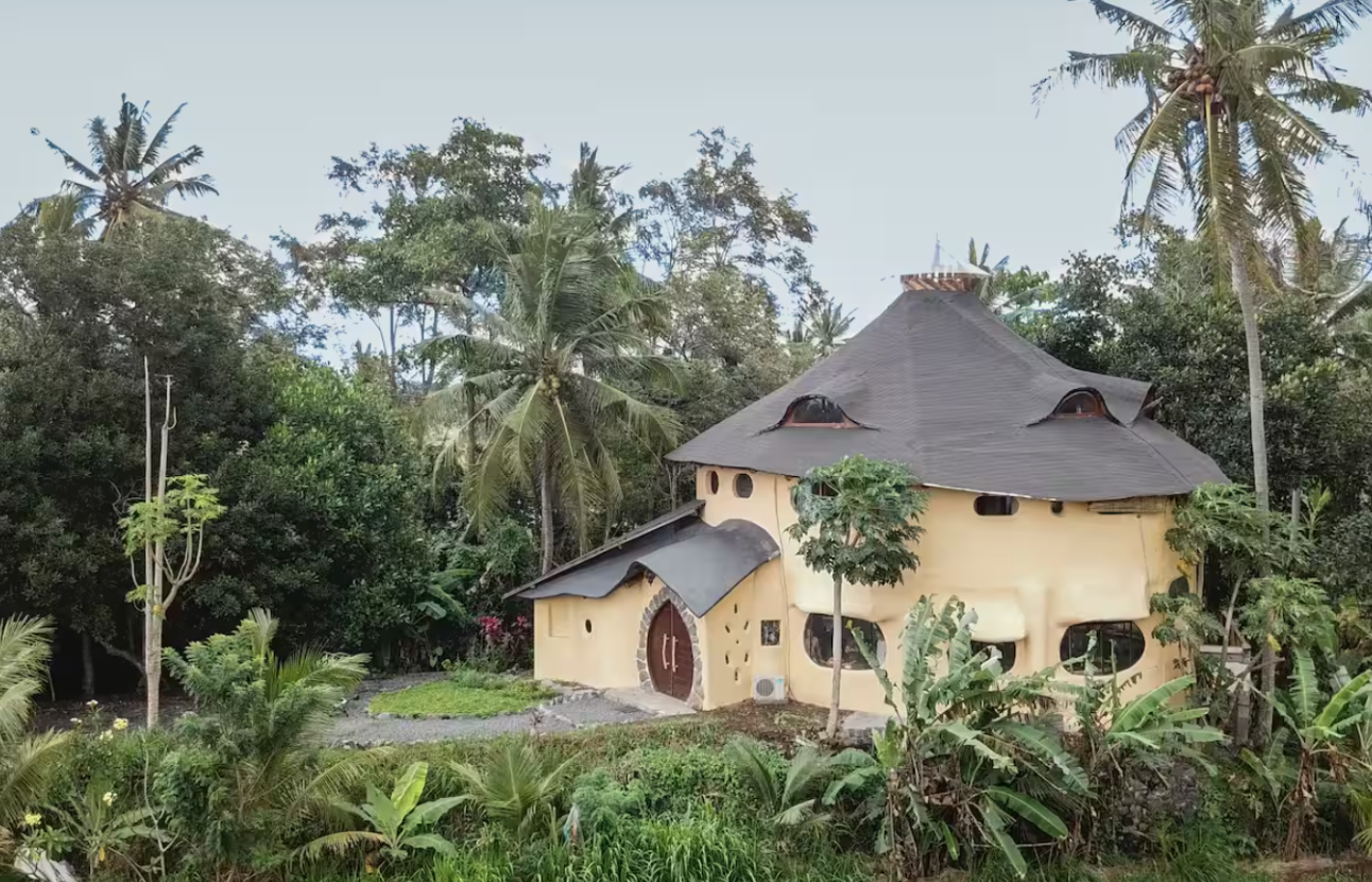 A whimsical house with organic, curved architecture, surrounded by lush tropical trees and plants.
