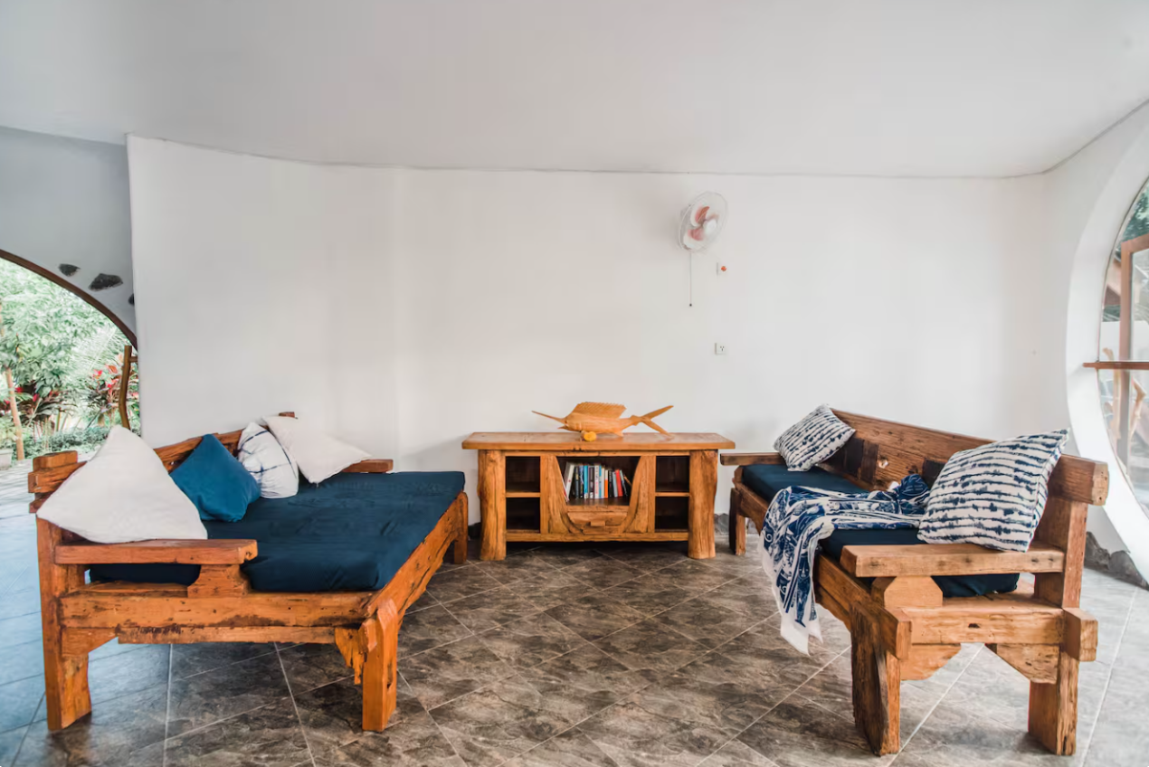 Living room with wooden furniture, white walls, and a round window revealing greenery outside.