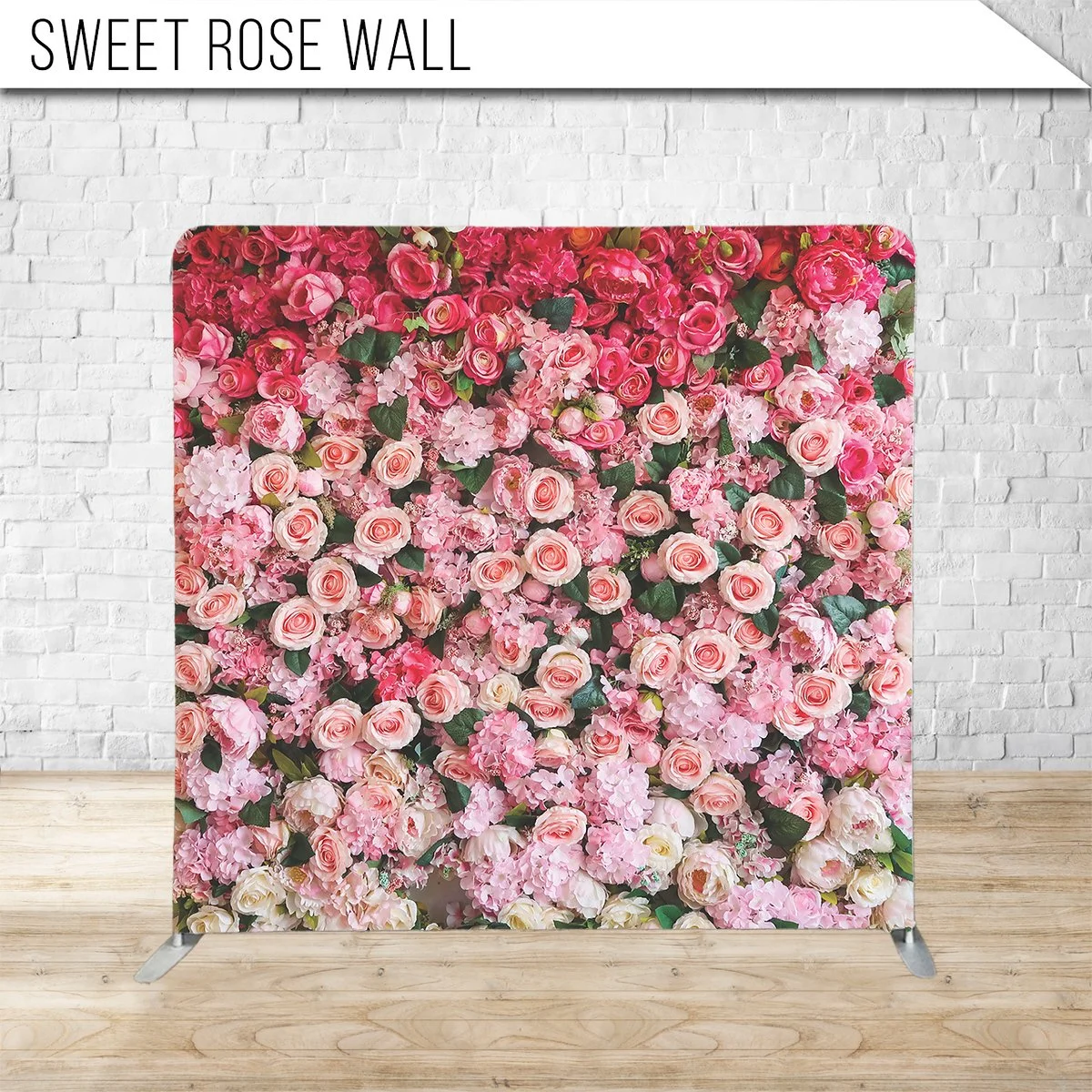 A floral wall display filled with pink and white roses, hydrangeas, and other pink flowers in front of a white brick wall with the sign 'Sweet Rose Wall' at the top.