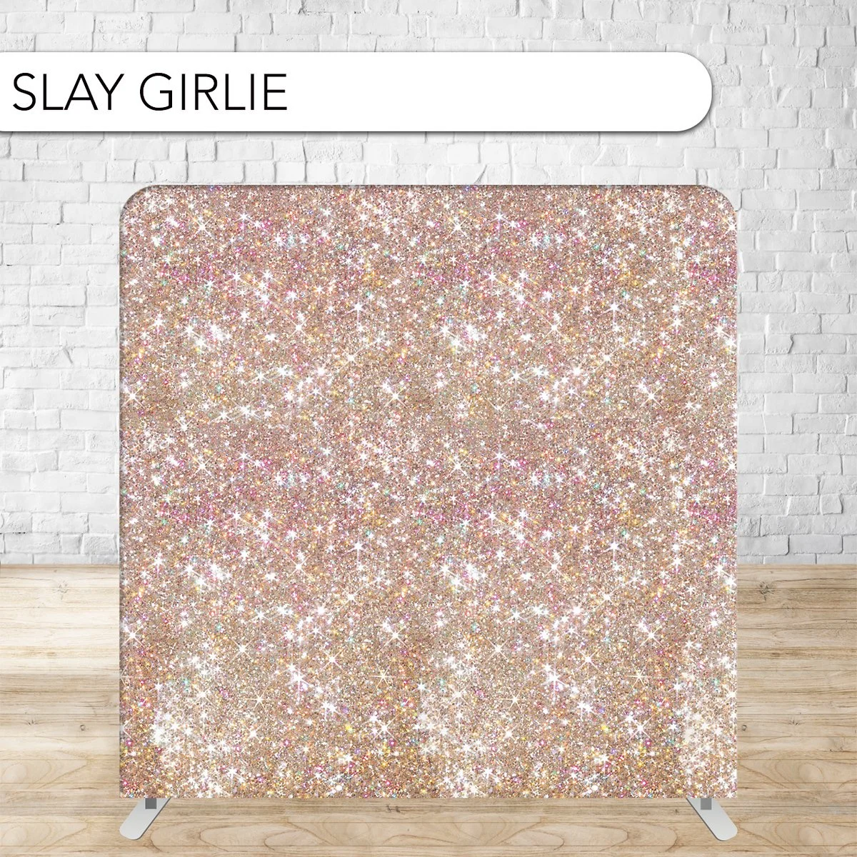 A glittery, sparkling pink and gold backdrop with the words "SLAY GIRLIE" on a white banner, set against a white brick wall and wooden floor.