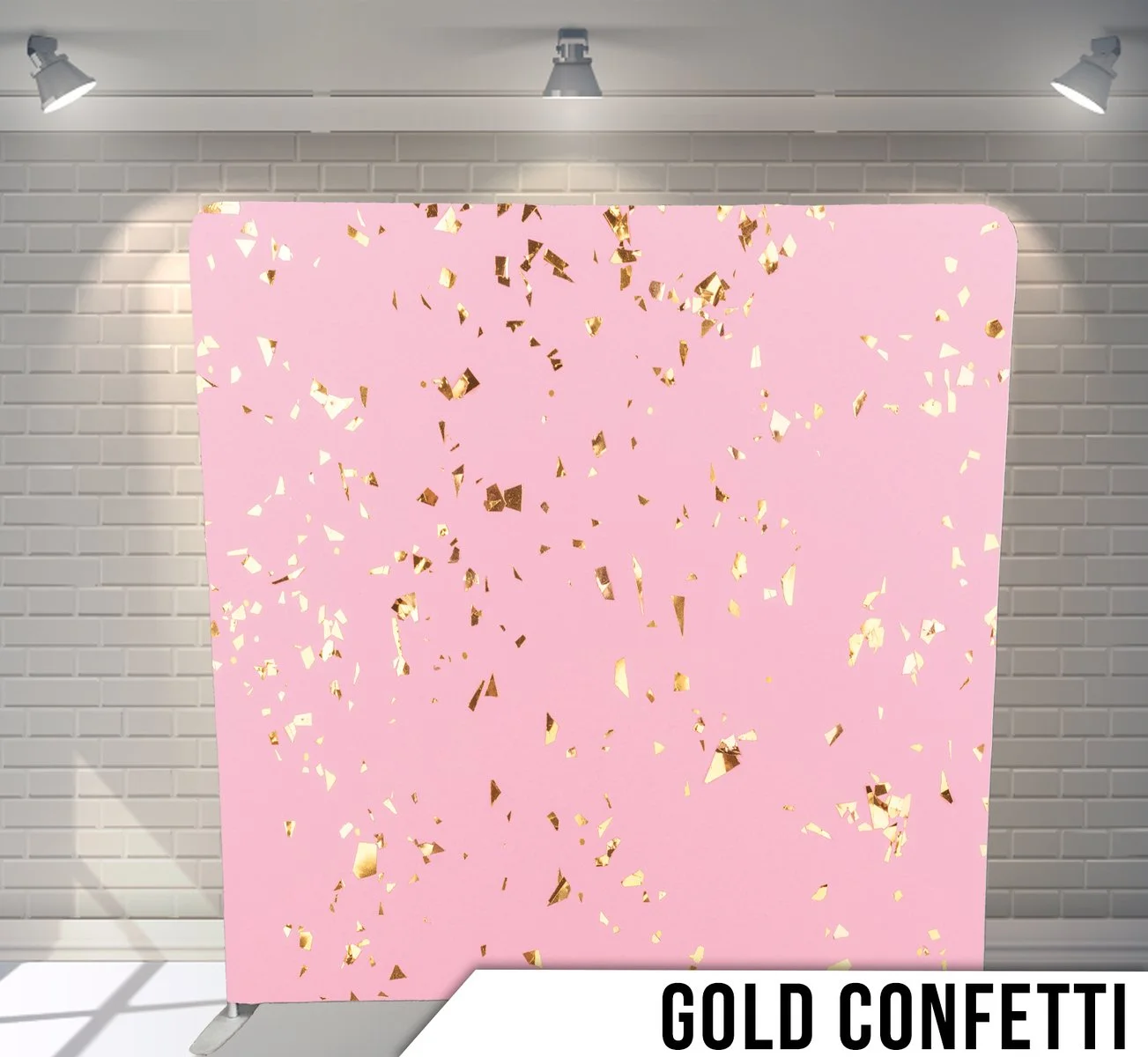 Pink backdrop with gold confetti scattered on it, set against a white brick wall with overhead spotlights.