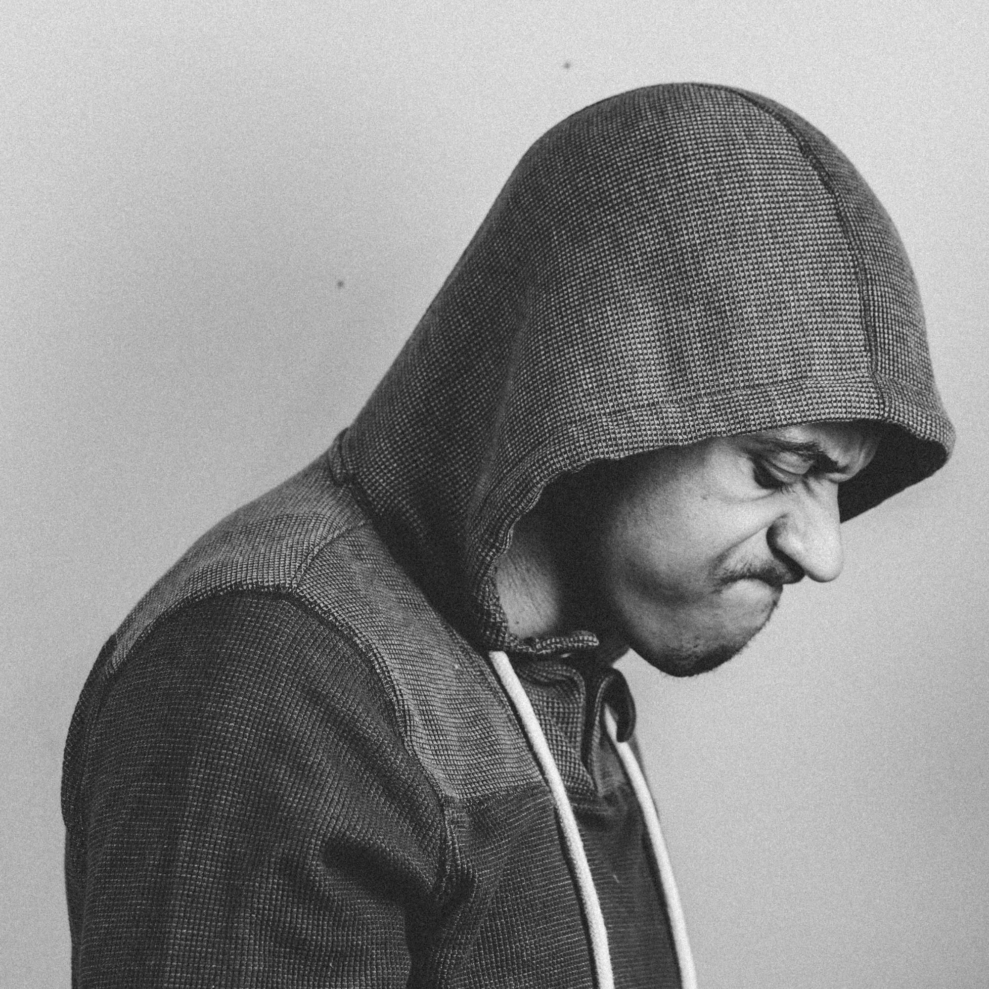 A black-and-white close-up of a person wearing a checkered hoodie, with the hood pulled over their head, looking downward.