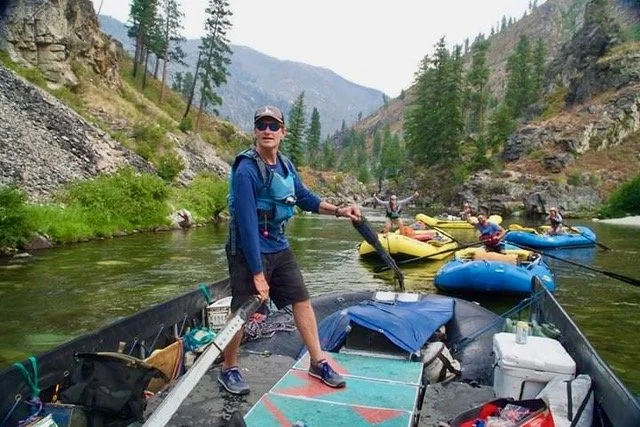 People kayaking in a river surrounded by mountains and trees.