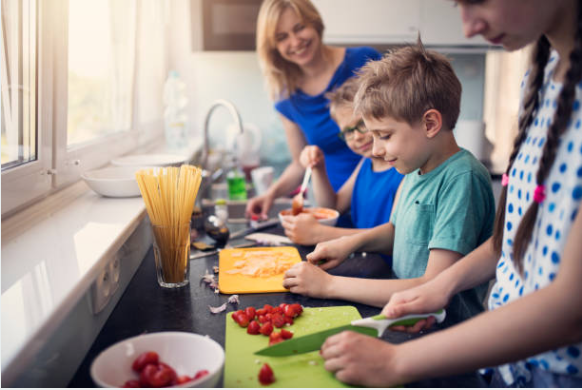 A family enjoys making pasta and preparing strawberries in the kitchen.