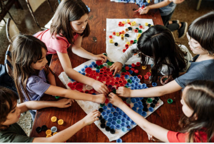 Children playing the game Connect Four with colorful plastic bottle caps on a wooden table.