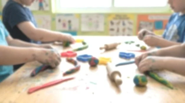 Children playing with colorful clay and clay tools at a table in a classroom.