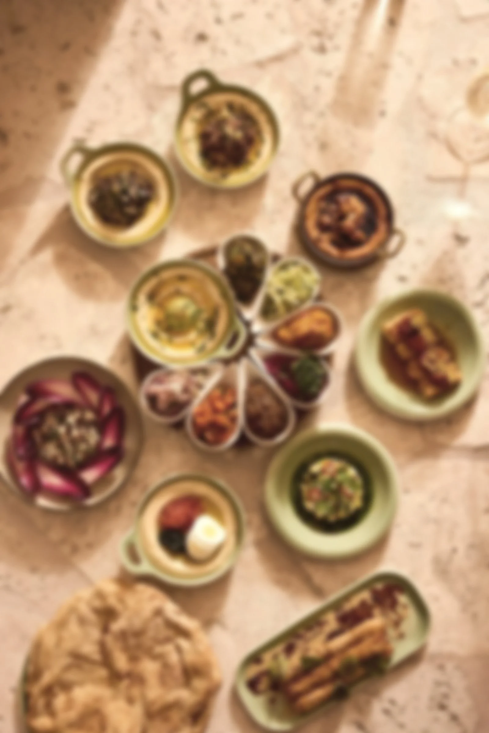Various small bowls with different types of food, including dips, salads, and snacks, arranged on a table. There are also some sandwiches or wraps and a plate with a cooked dish.
