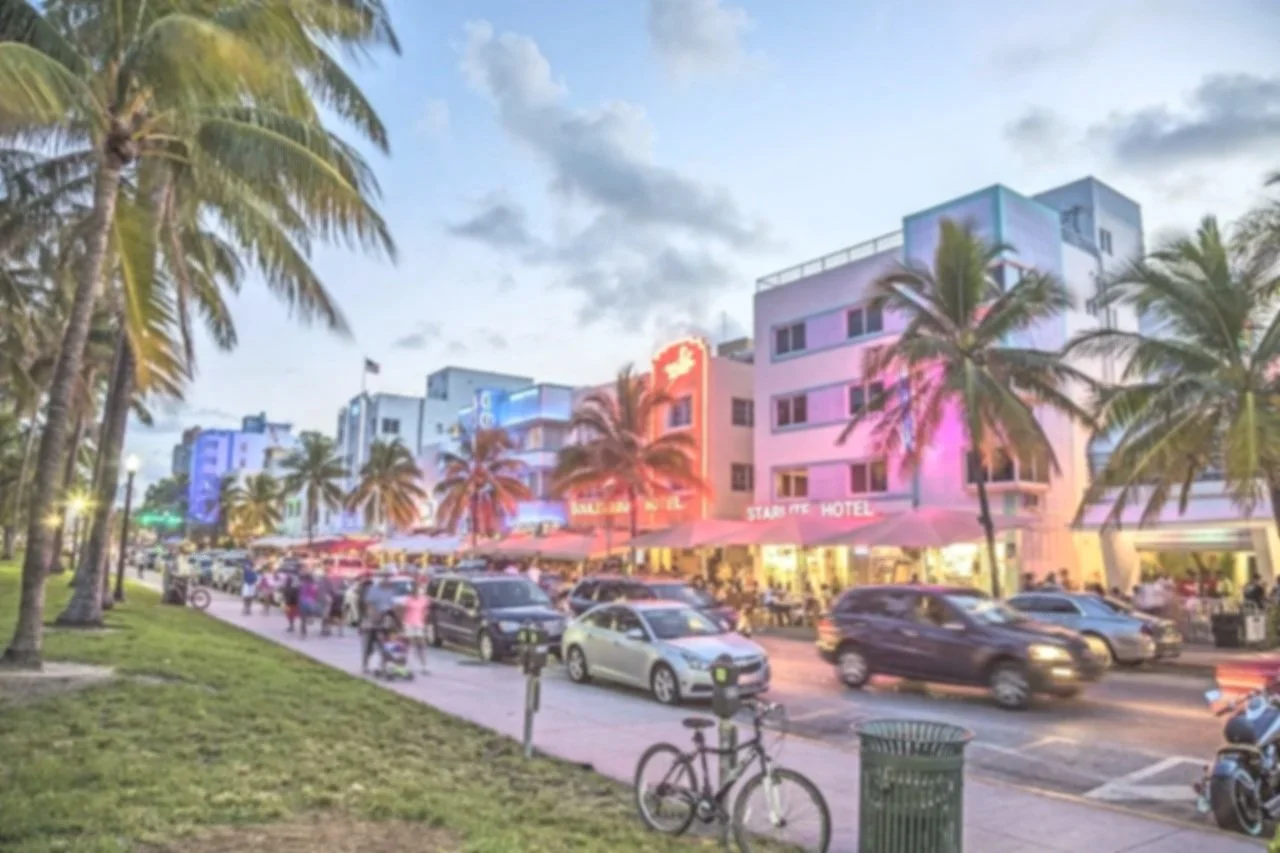Night view of a busy street with colorful buildings, palm trees, and cars, featuring a hotel with a neon sign reading 'Star Fish Hotel' and people walking along the sidewalk.