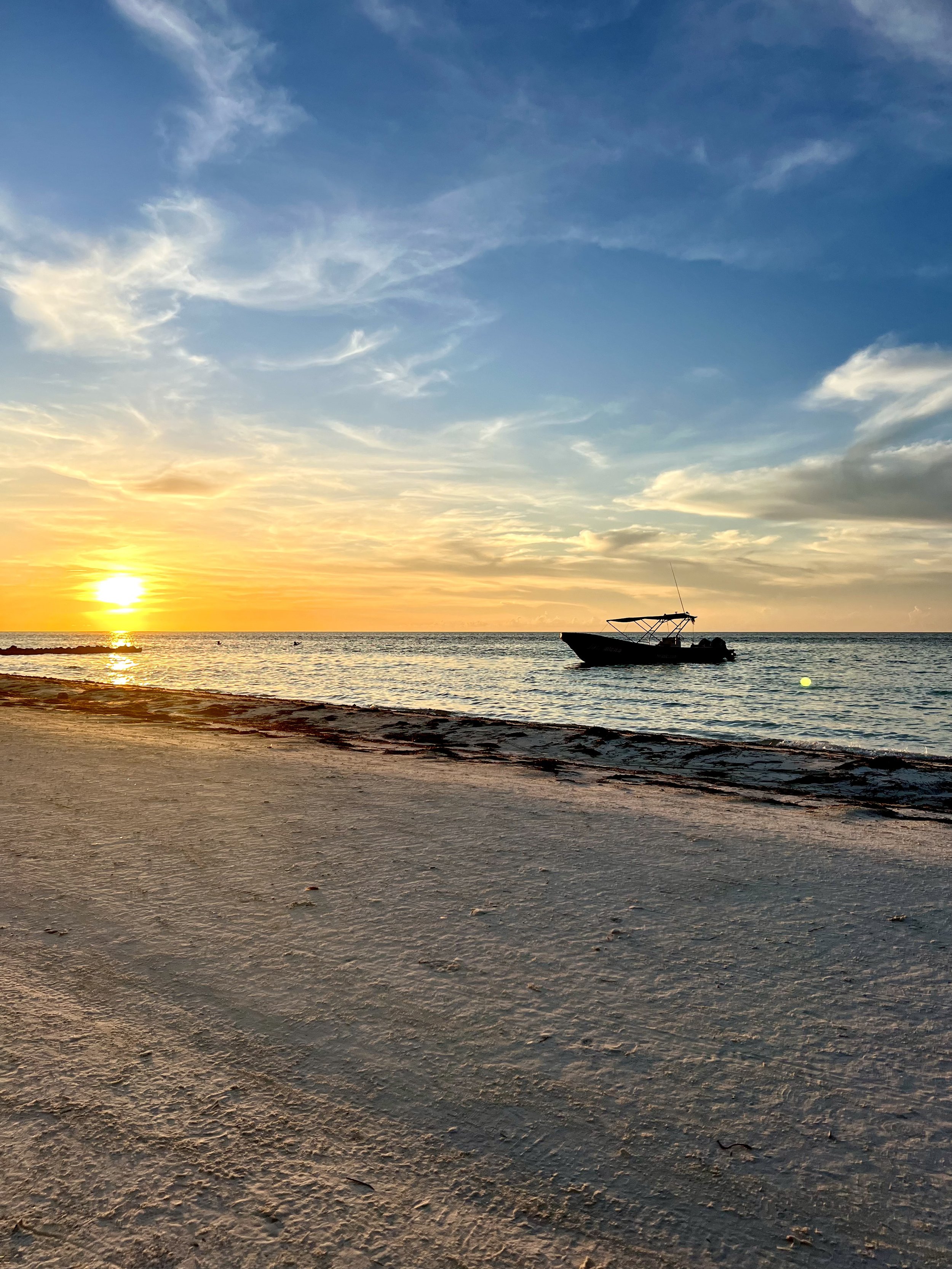 Coucher de soleil sur une plage avec un bateau à moteur dans l'eau, ciel partiellement nuageux, sable au premier plan.