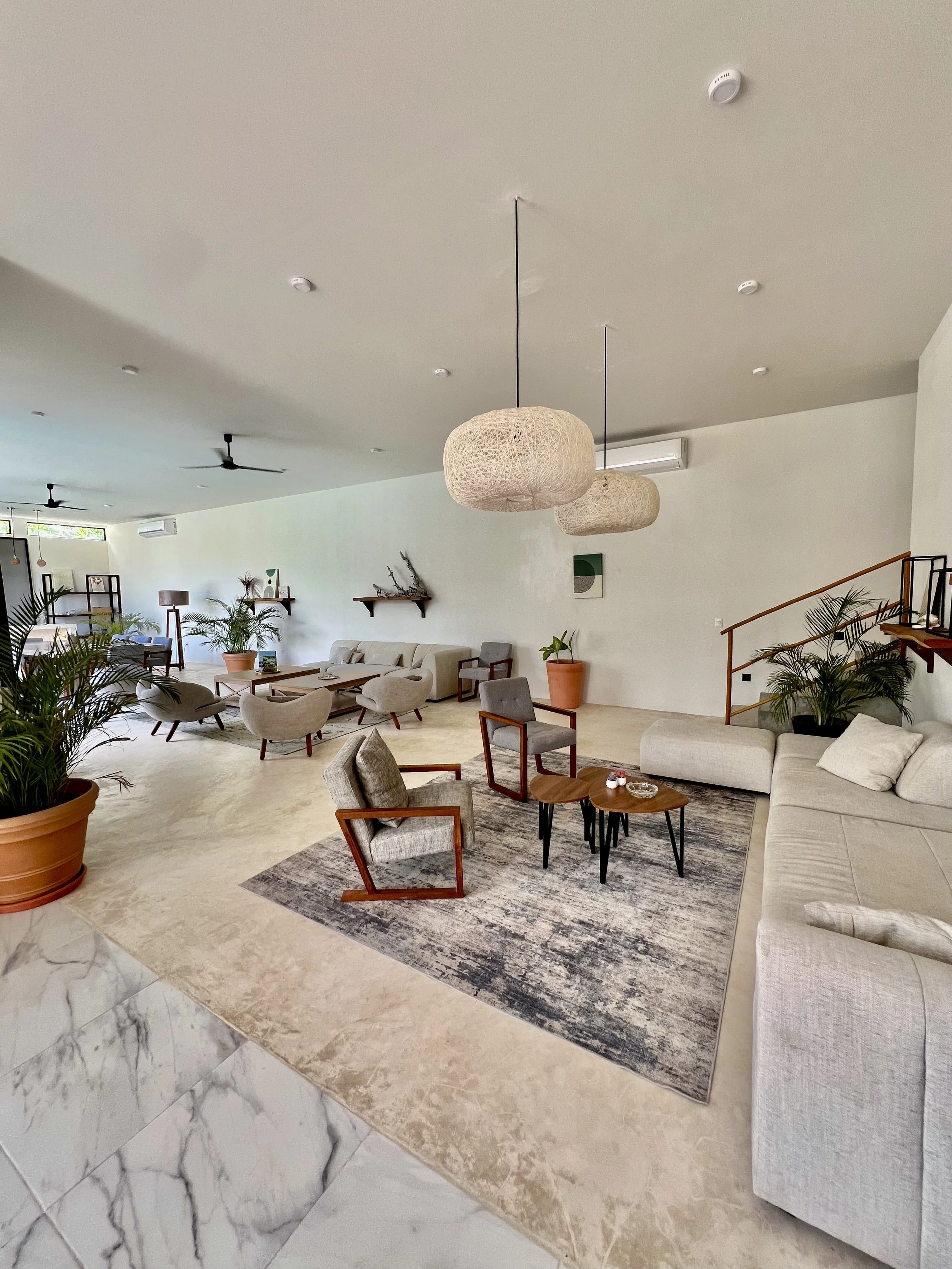 Salon blanc et beige avec plusieurs fauteuils, canapés, tapis, plantes en pot, lampes suspendues en osier, murs décorés avec des étagères et des œuvres d'art