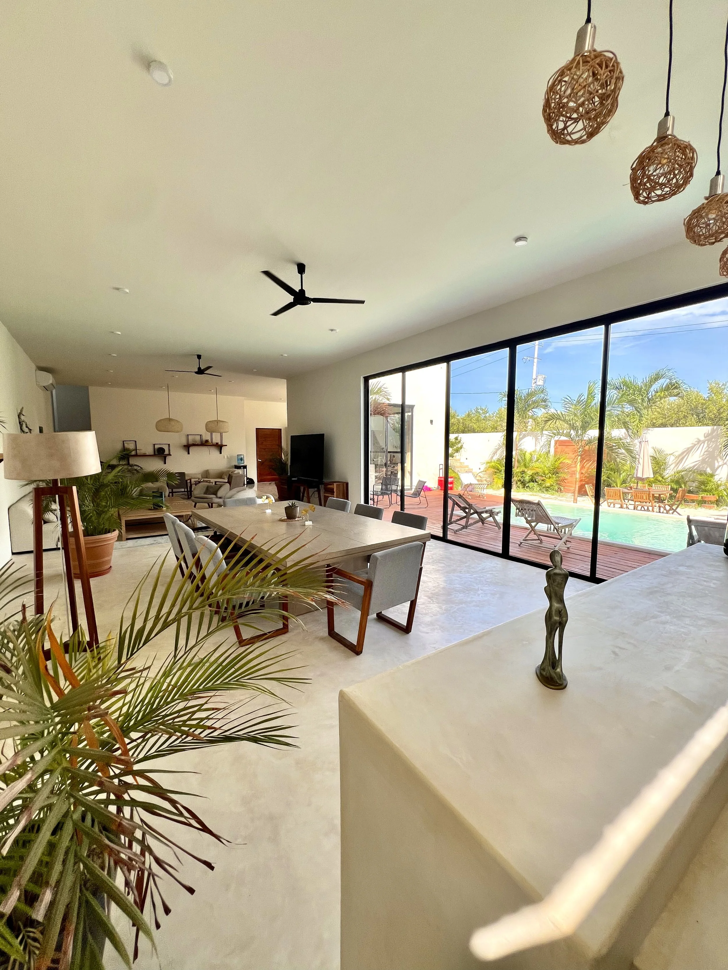 Intérieur d'une salle à manger lumineuse avec une grande table, des chaises, une cheminée et une télévision, avec à l'extérieur une piscine et un patio.