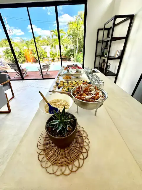 Buffet de petit déjeuner avec aliments variés, plantes et vue sur un jardin depuis une grande fenêtre