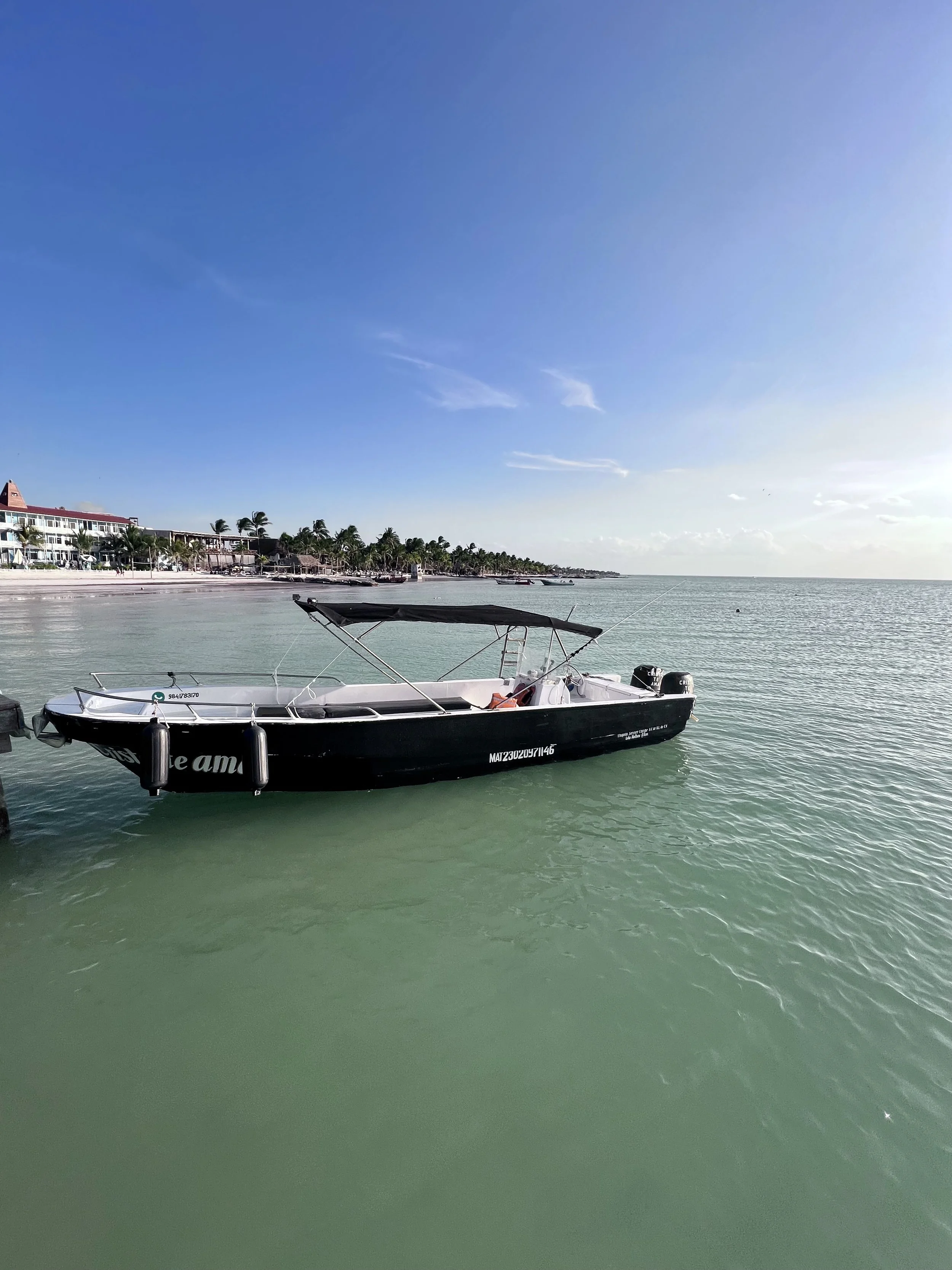 Bateau noir amarré au quai avec un ciel bleu clair et une mer calme, côté station balnéaire en arrière-plan.
