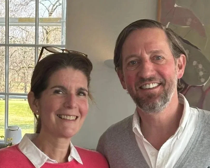 Bildausschnitt von einem lächelnden Mann und einer lächelnden Frau, die nebeneinander stehen und vor einem Fenster stehen.